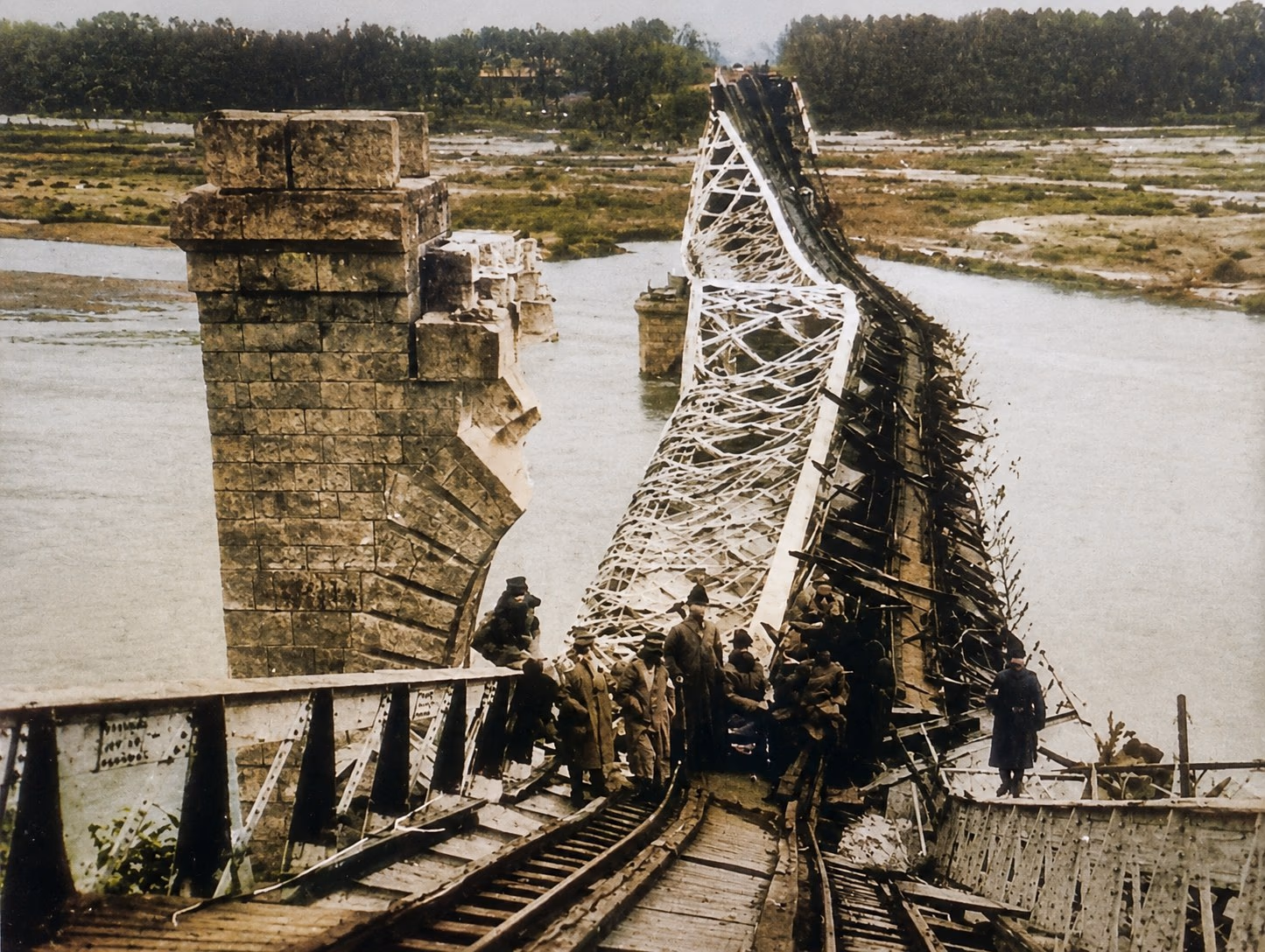 Podul Anghel Saligny de la Cosmești după dinamitarea din 2 august 1917 — structura metalică prăbușită peste Siret, pilonii de piatră încă în picioare, soldați pe ruine. Fotografie de arhivă, colorizată.
