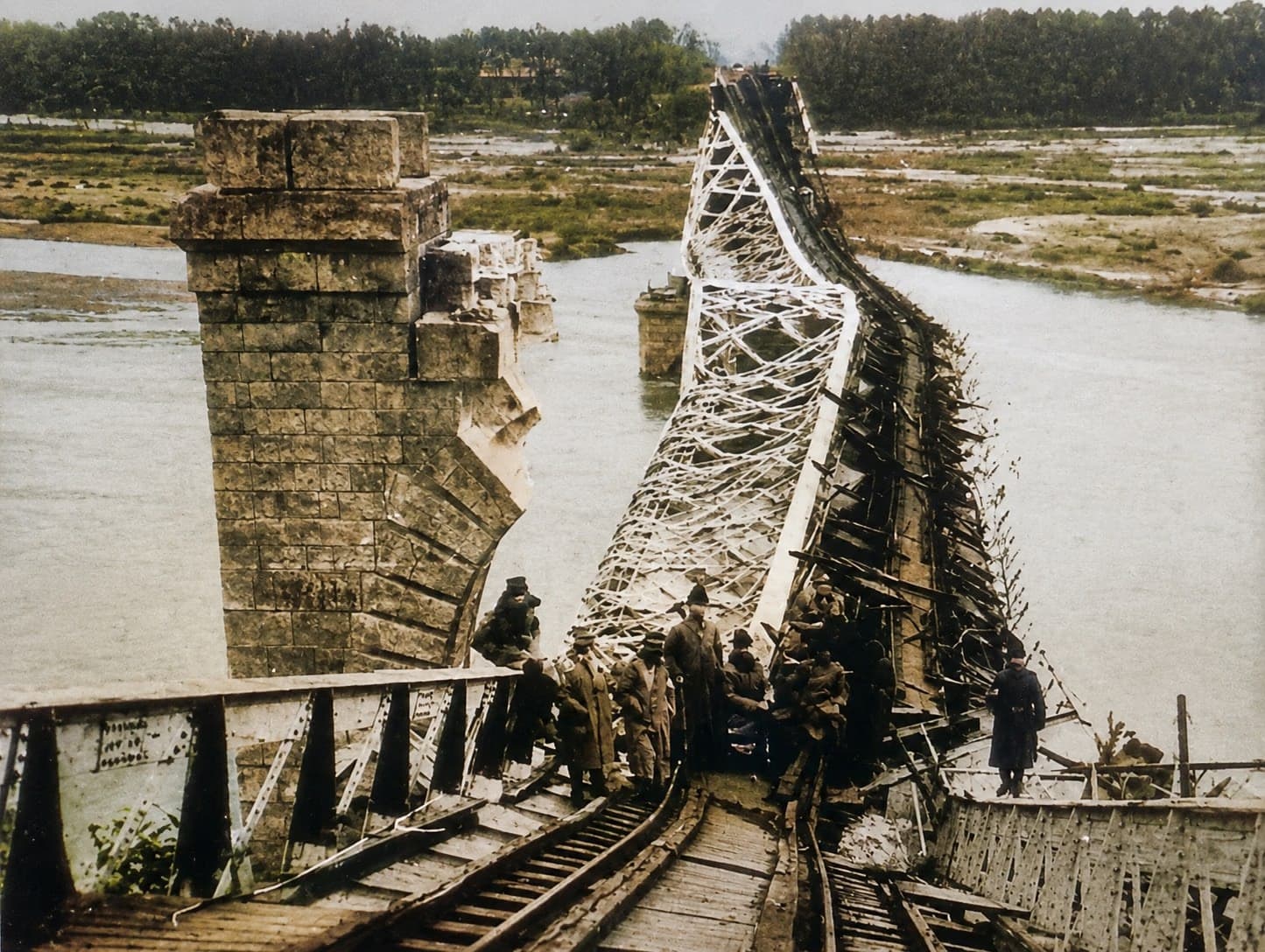 Podul Anghel Saligny de la Cosmești după dinamitarea din 2 august 1917 — structura metalică prăbușită peste Siret, pilonii de piatră încă în picioare, soldați pe ruine. Fotografie de arhivă, colorizată.