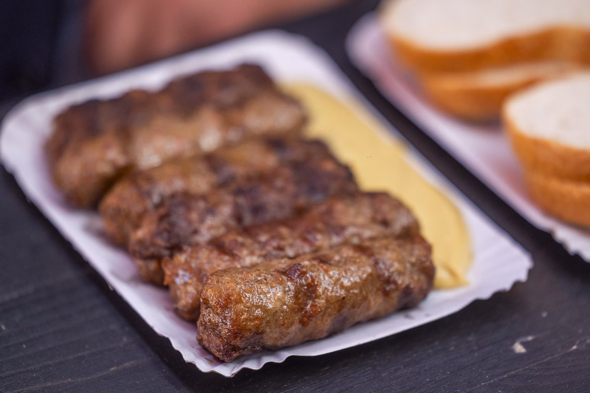 Șase mici aliniați pe muștar dulce, pe tăviță albă de carton, lângă felii de pâine din franzelă la Terasa Obor.