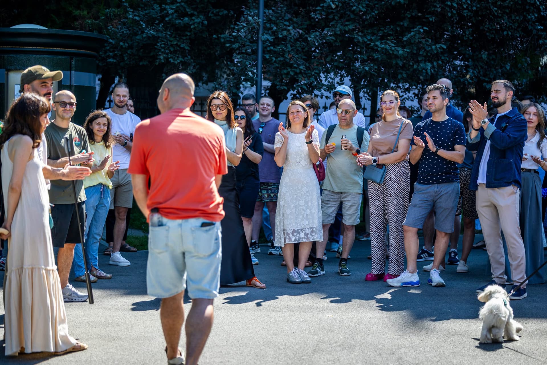 Endi háttal a kamerának, tapsoló csoport veszi körül — a fehér kutya a keret szélén