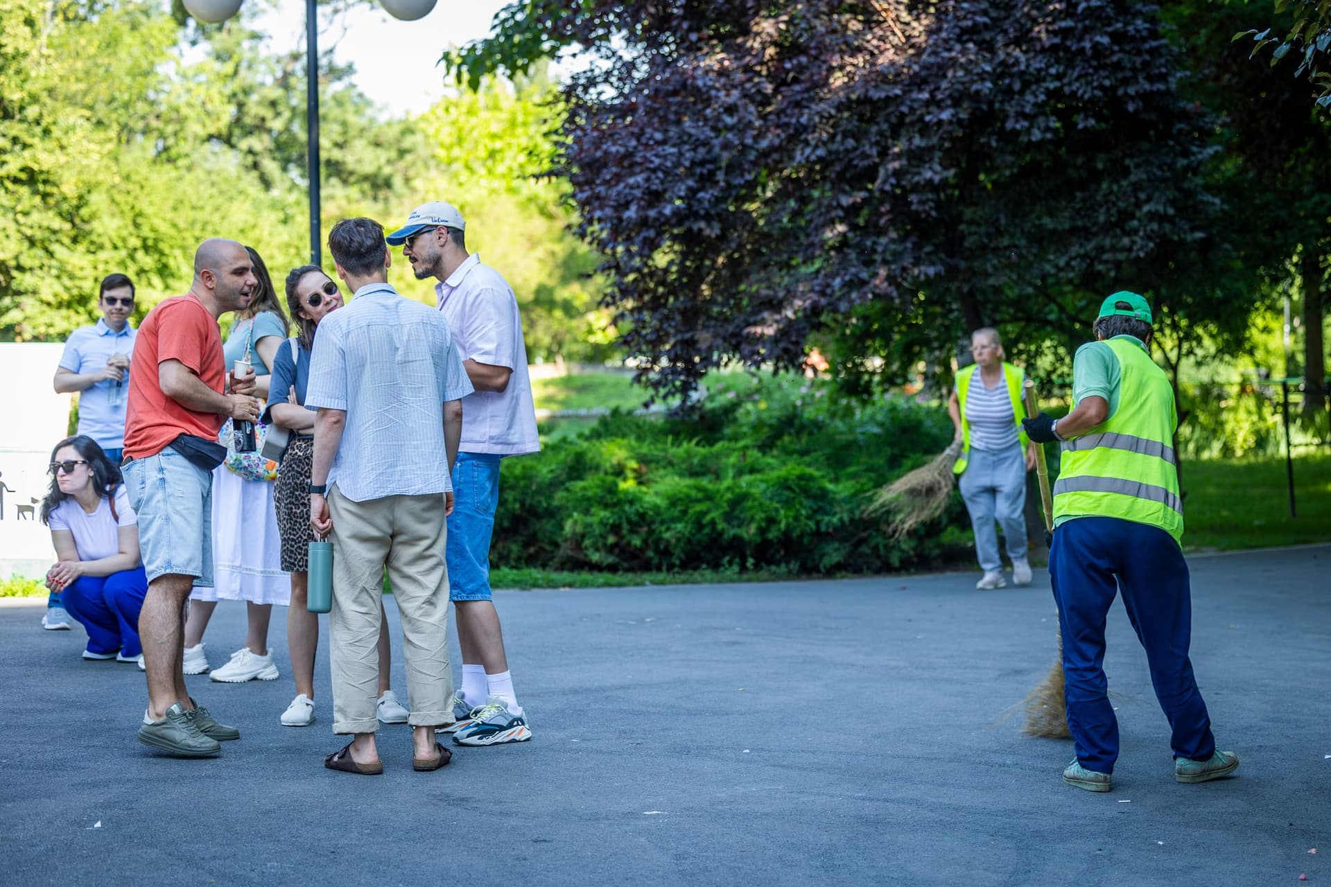 Egy kis csoport áll a Cișmigiu kapujánál, miközben egy városi takarító halad az allén