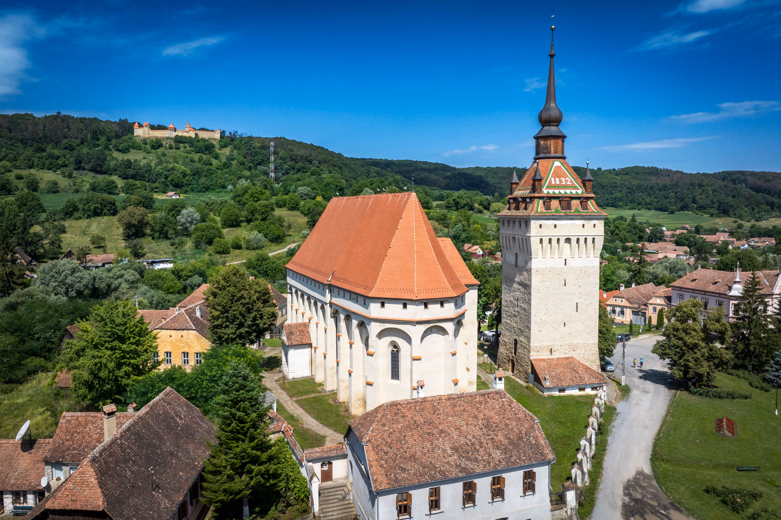 Biserica și clopotnița din Saschiz, cu cetatea vizibilă în depărtare pe deal