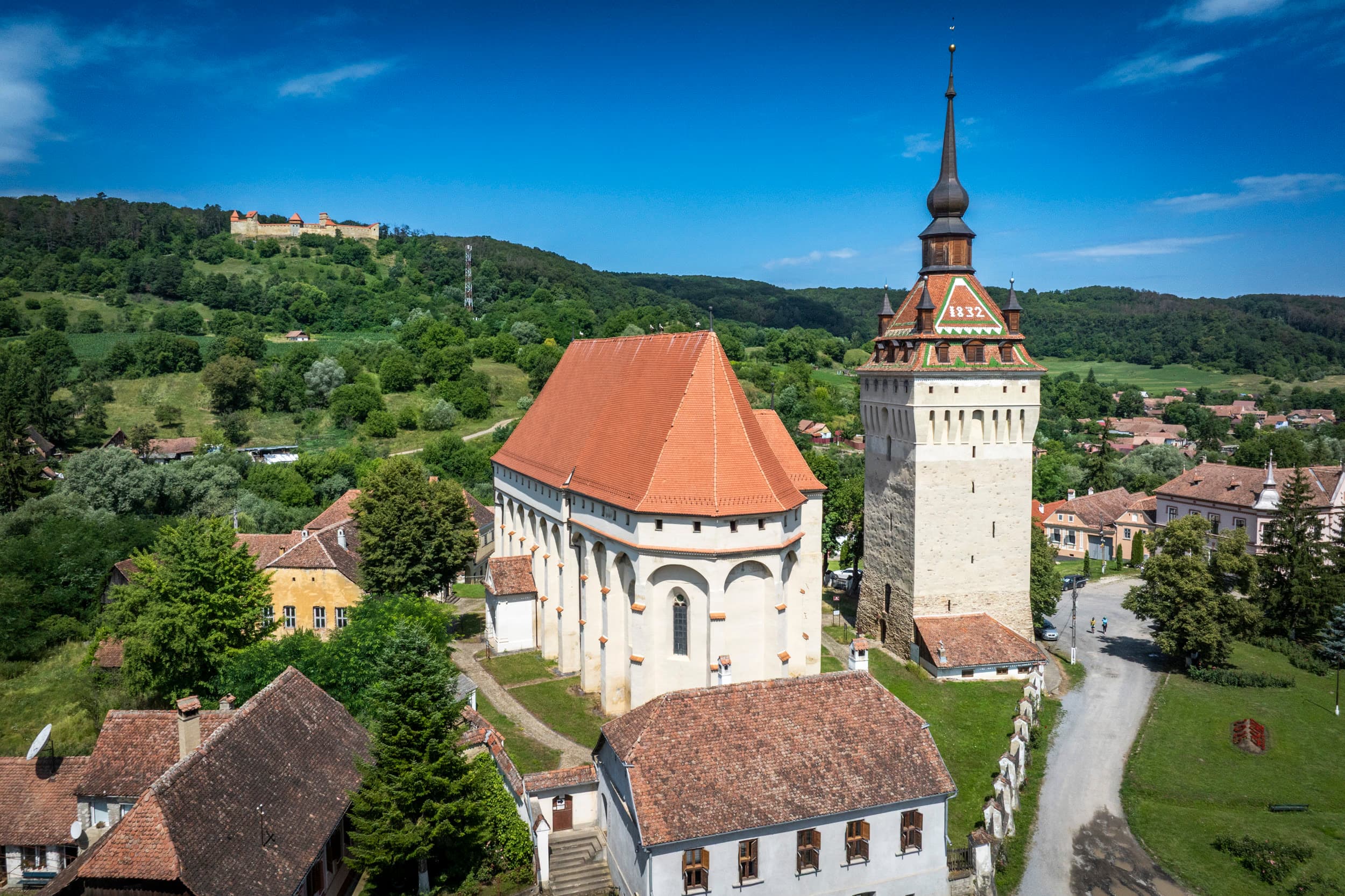 Biserica și clopotnița din Saschiz, cu cetatea vizibilă în depărtare pe deal