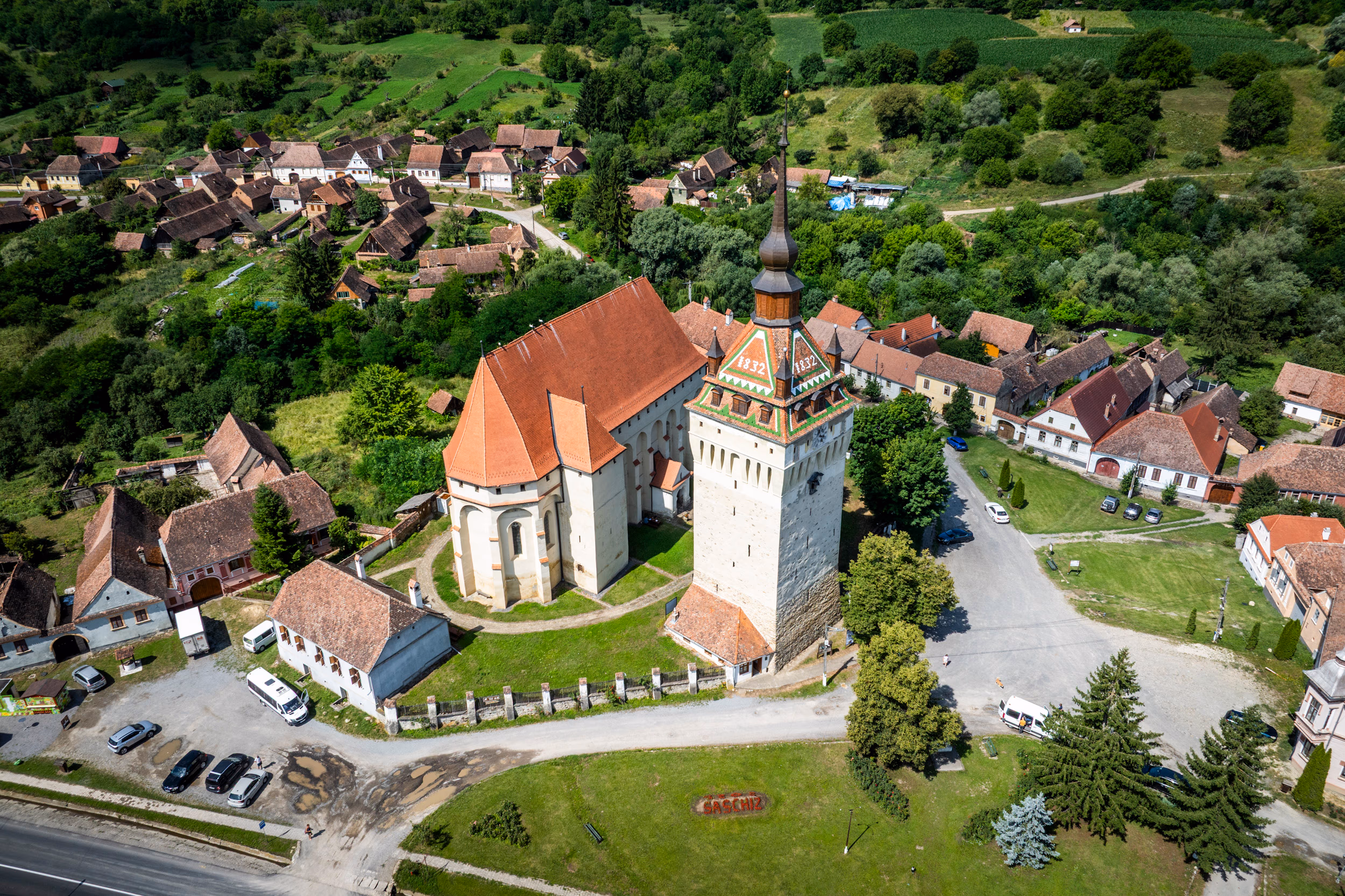 Biserica fortificată din Saschiz — vedere aeriană din spate, parcare în față, contraforturile gotice vizibile