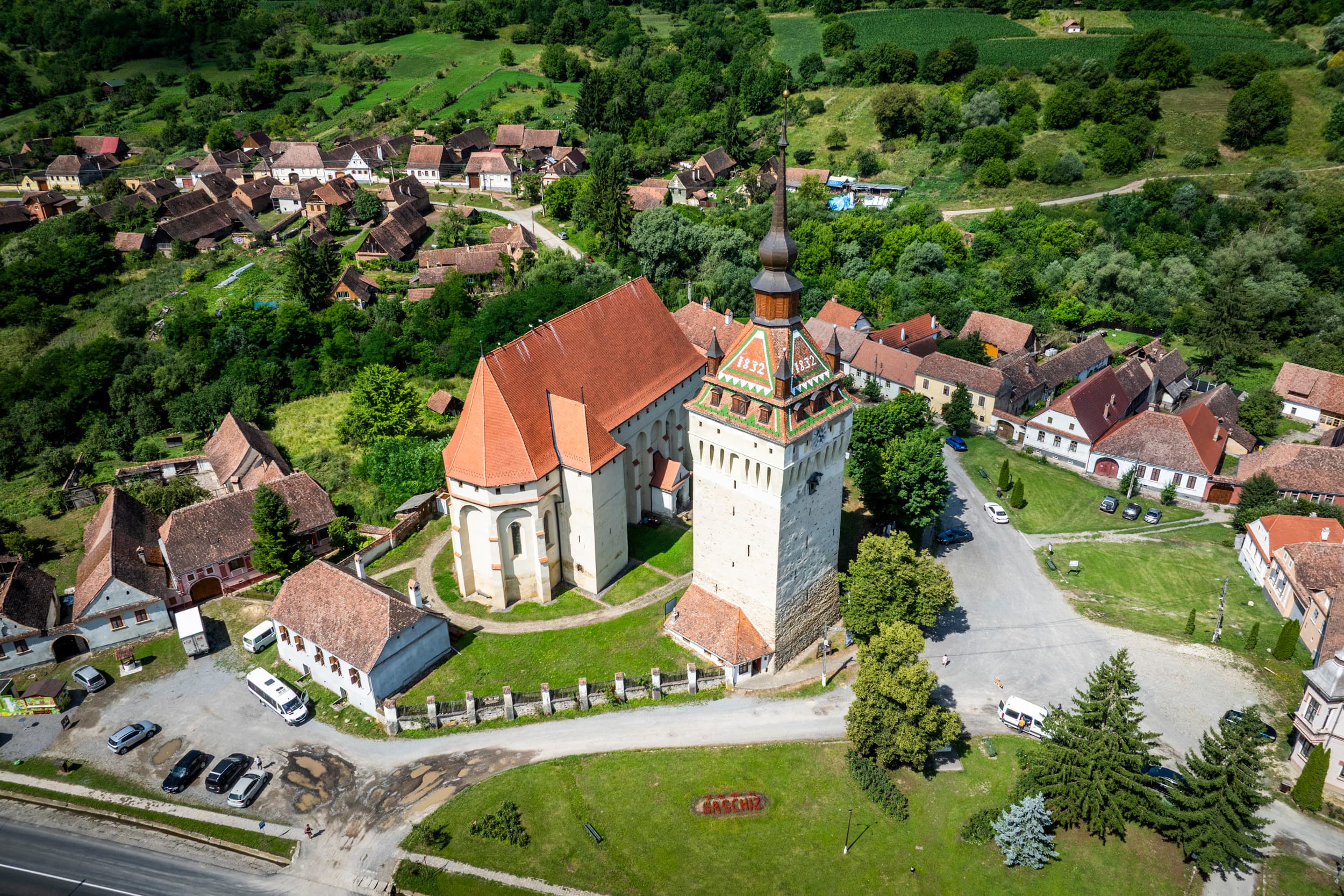 Biserica fortificată din Saschiz — vedere aeriană din spate, parcare în față, contraforturile gotice vizibile