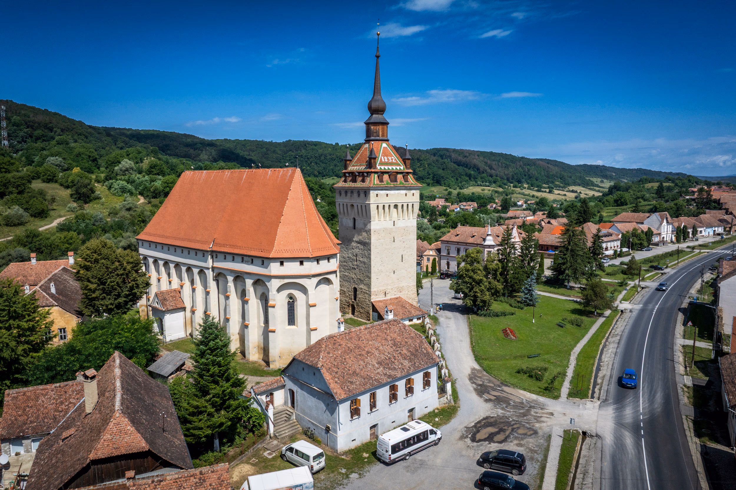 Biserica fortificată — vedere laterală cu DN13 în prim-plan, satul în depărtare