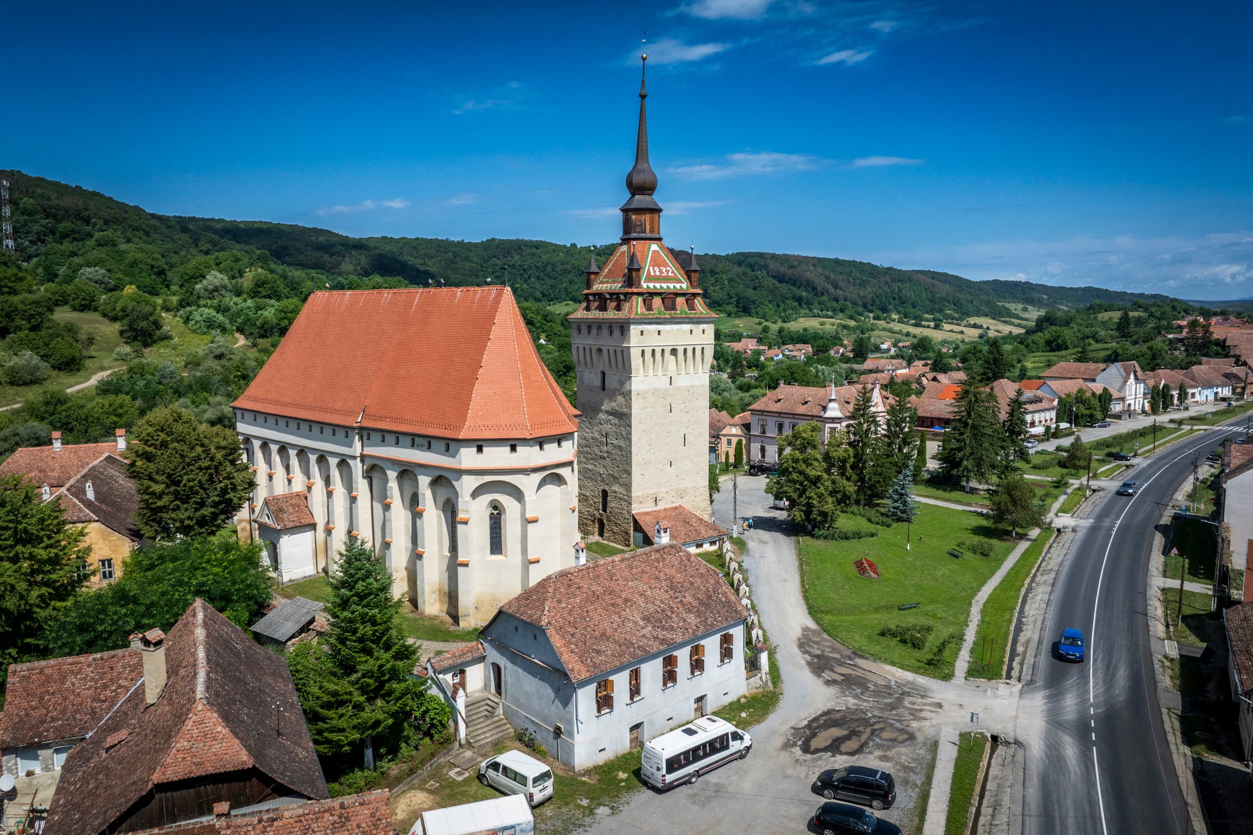 Biserica fortificată — vedere laterală cu DN13 în prim-plan, satul în depărtare