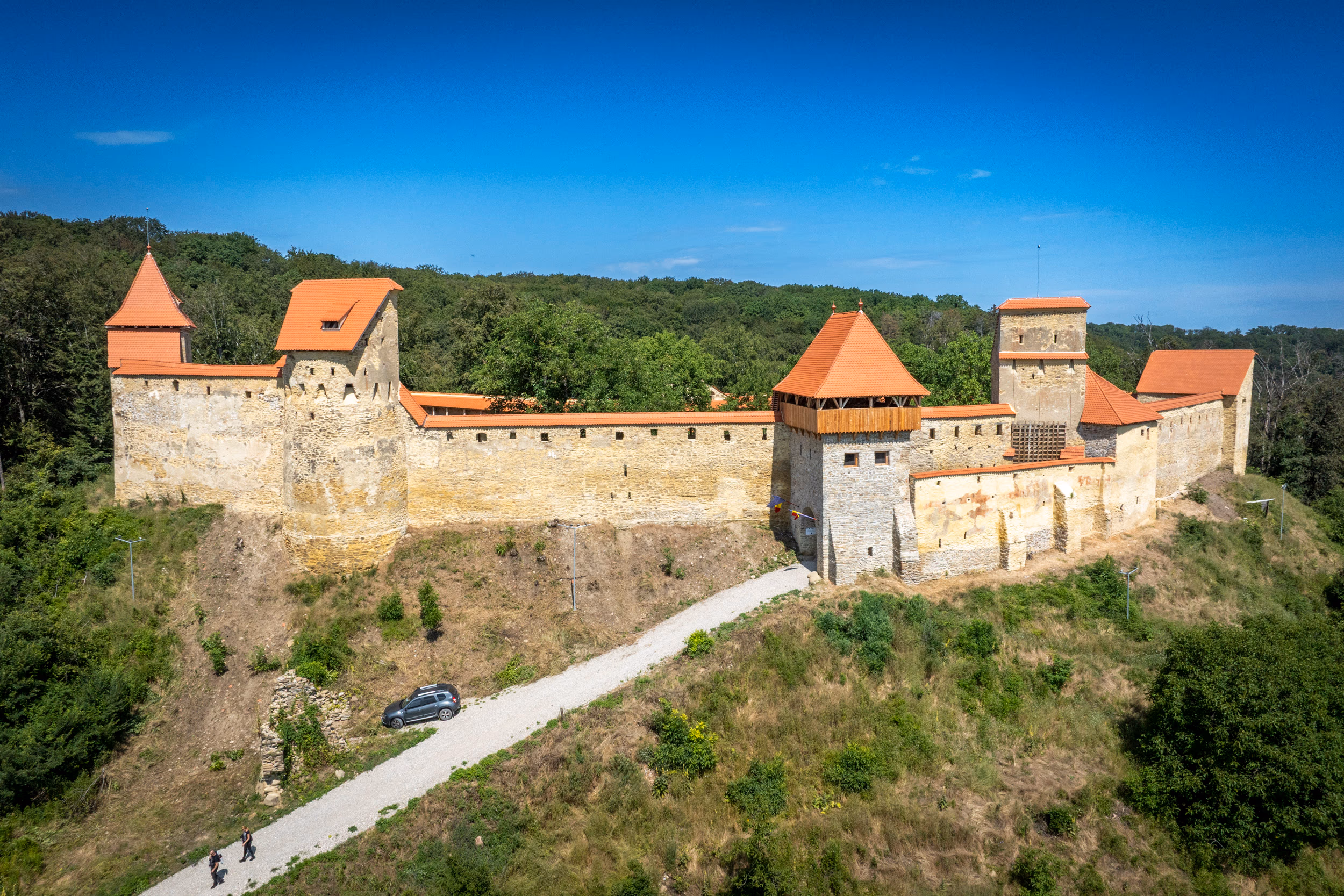 Cetatea Țărănească de pe Dealul Cetății — turnuri cu acoperiș roșu, ziduri din piatră de carieră, în mijlocul pădurii