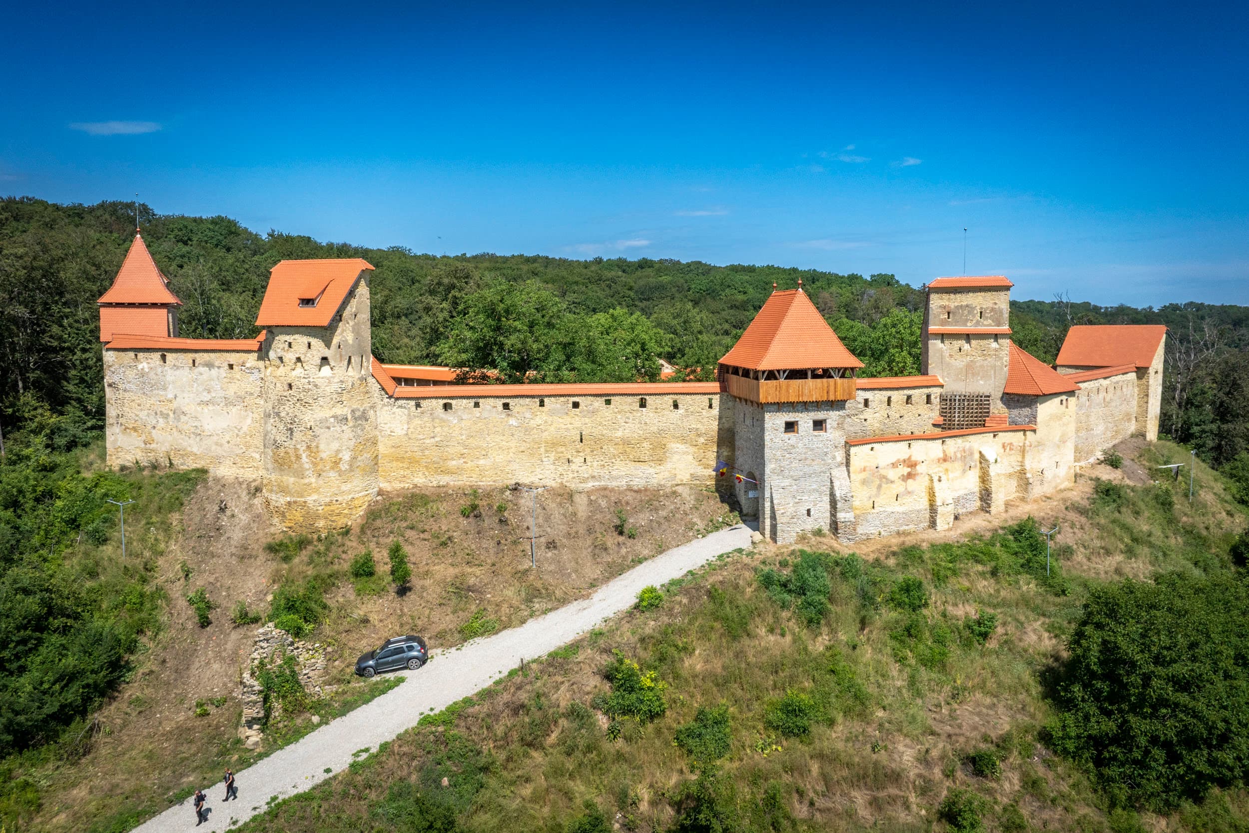 Cetatea Țărănească de pe Dealul Cetății — turnuri cu acoperiș roșu, ziduri din piatră de carieră, în mijlocul pădurii