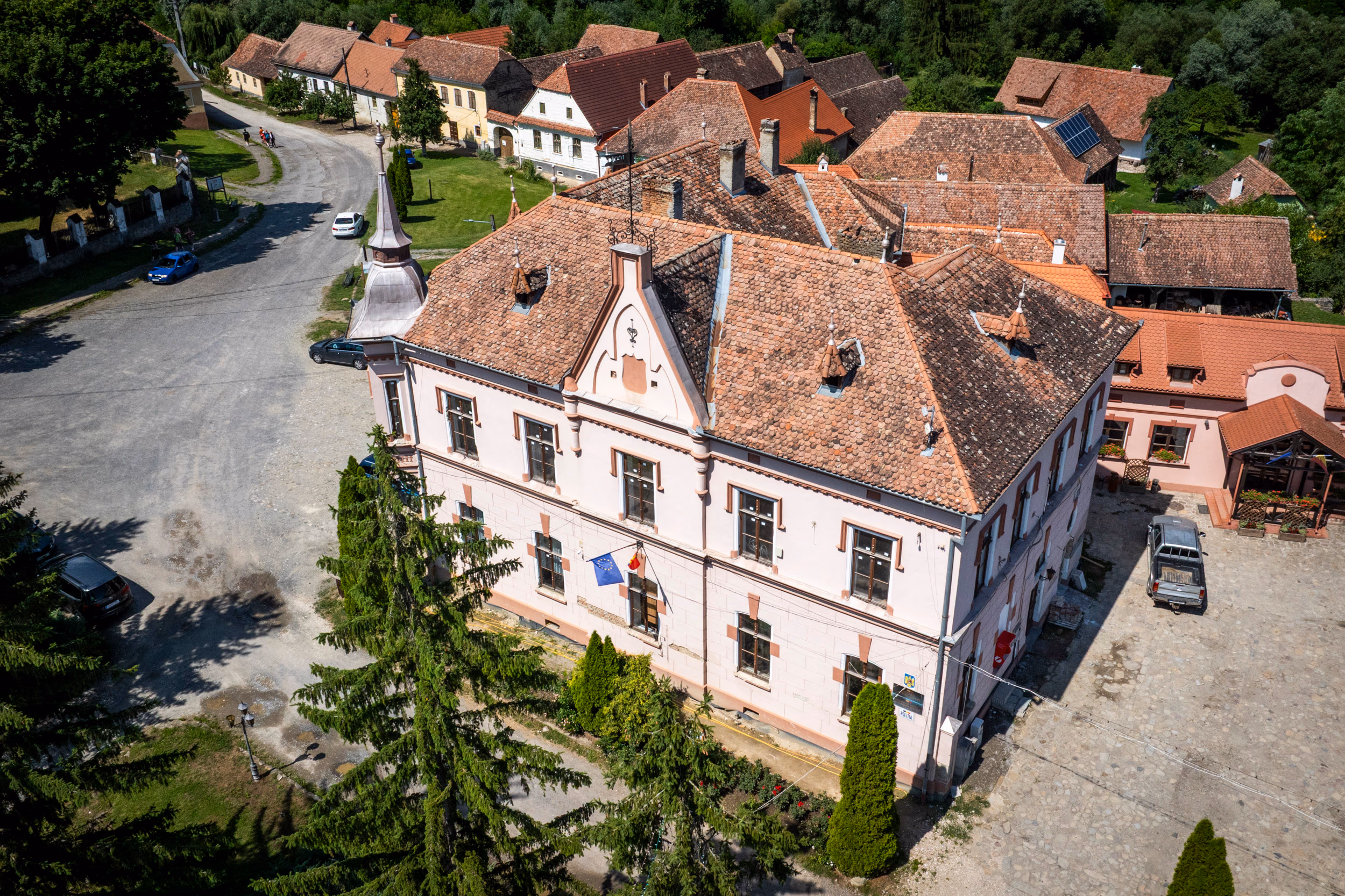 Primăria comunei Saschiz — clădire roz cu turnuleț de ceas, drapel român, vedere aeriană