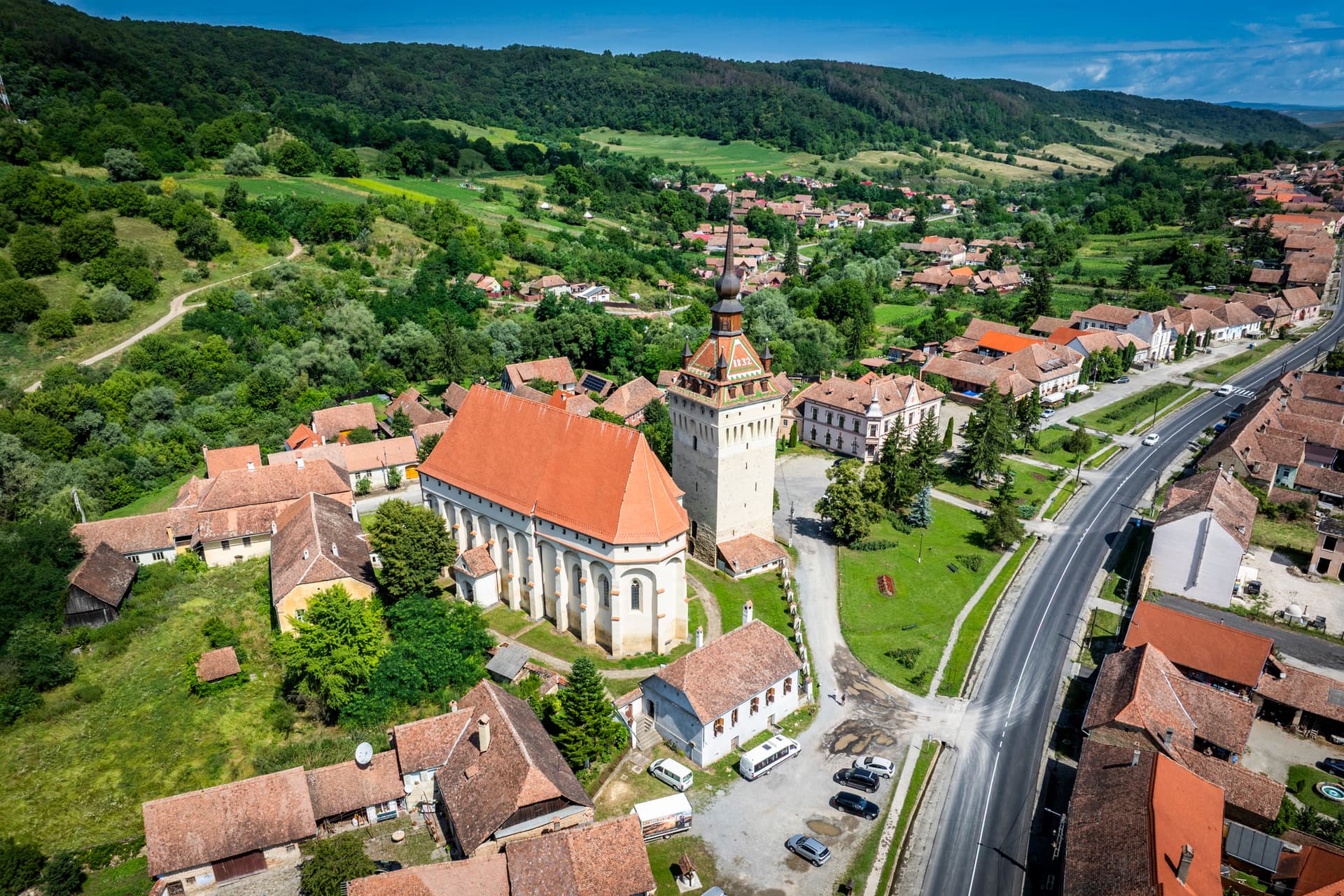 Vedere amplă a satului dinspre înălțime — DN13 trecând prin centru, casele săsești cu acoperiș roșu aliniate