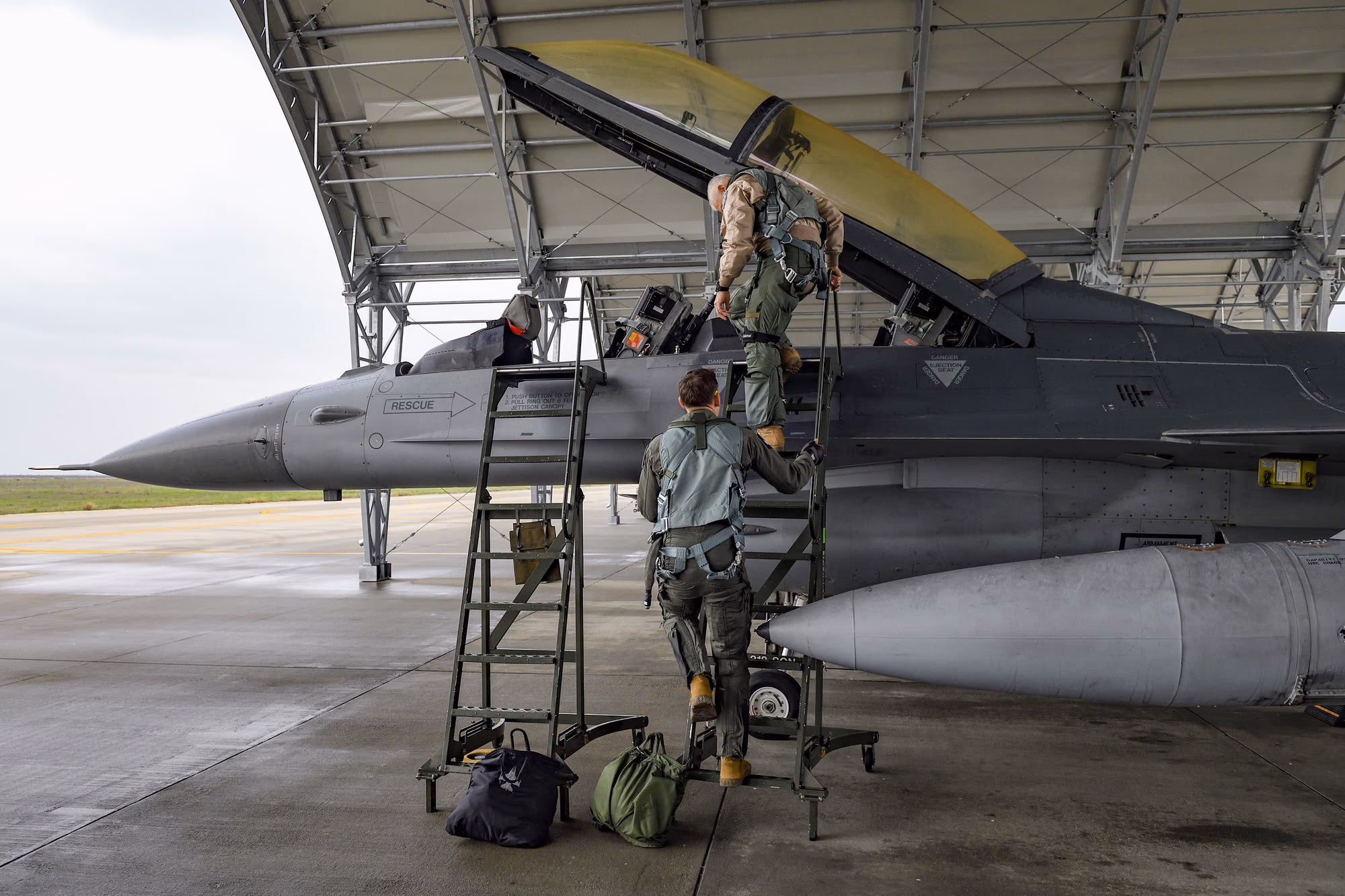 Két pilóta a Fetești-i EFTC hangárjában egy F-16 pilótafülkéjébe felmászva — teljes repülési felszerelésben