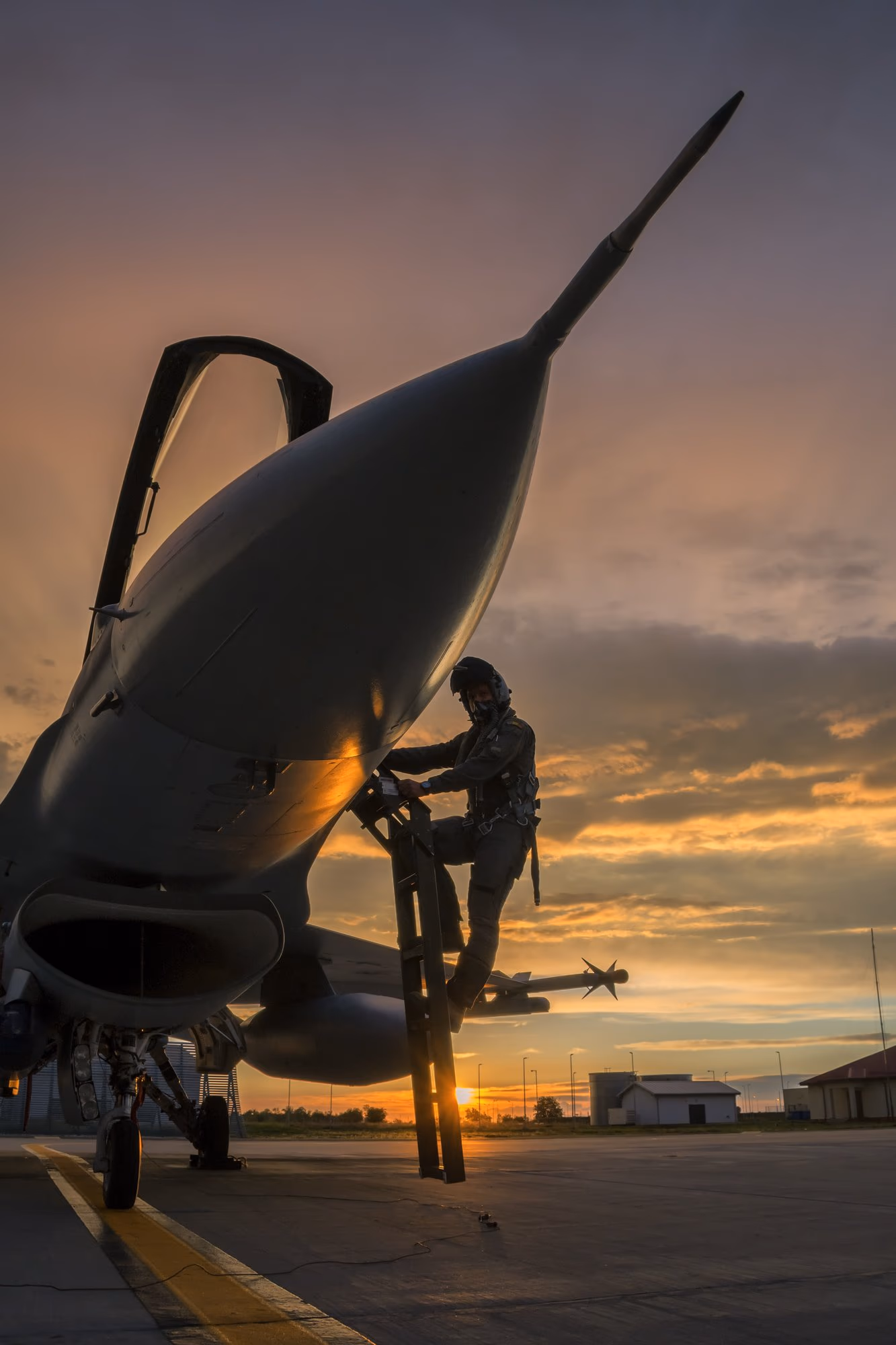 Román pilóta egy F-16 pilótafülkéjébe felmászva, a napnyugta fényében, egy légi bázison