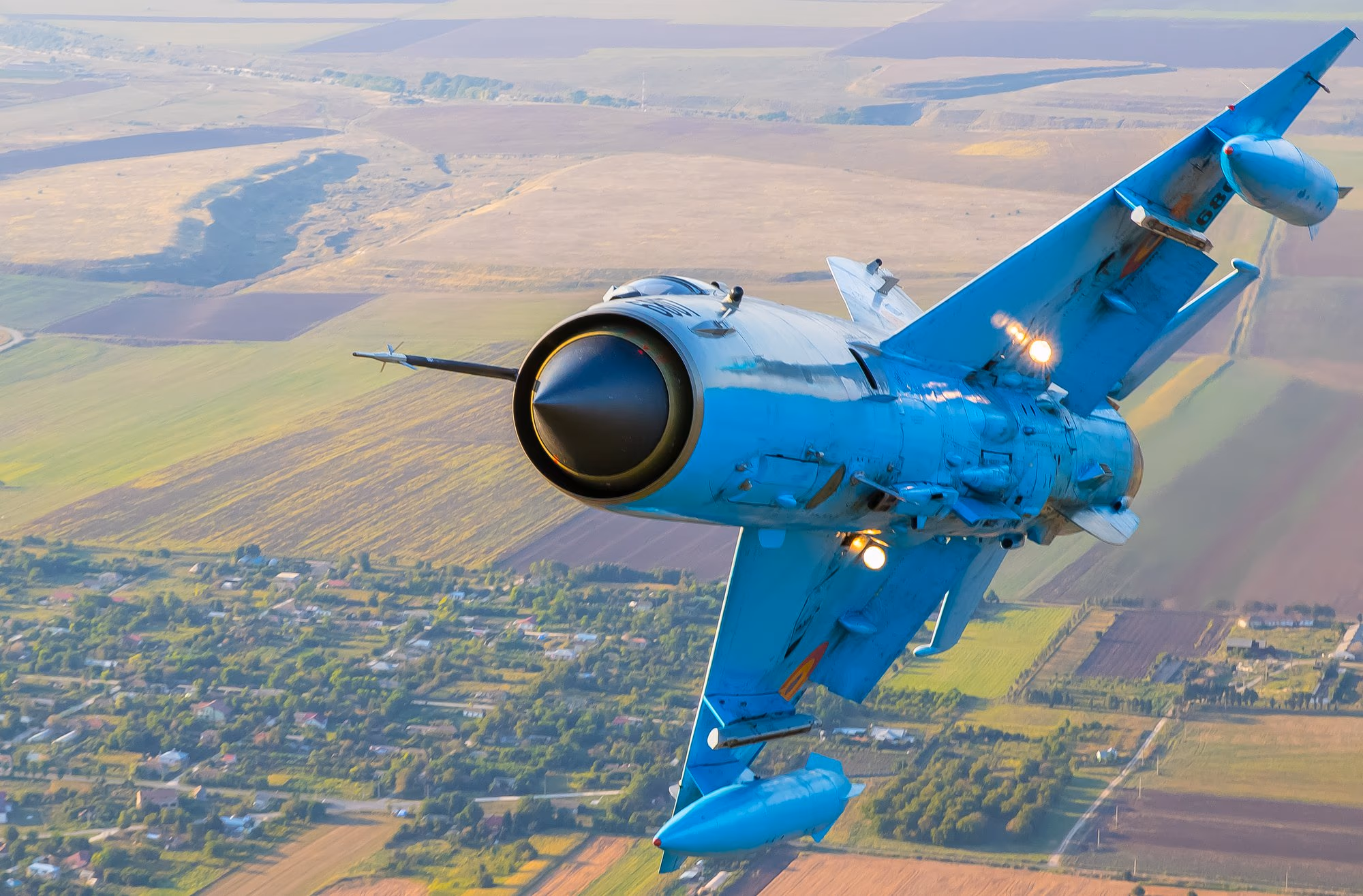 MiG-21 LanceR repülés közben — láthatóan kopott álcafestés a mezőgazdasági táj felett