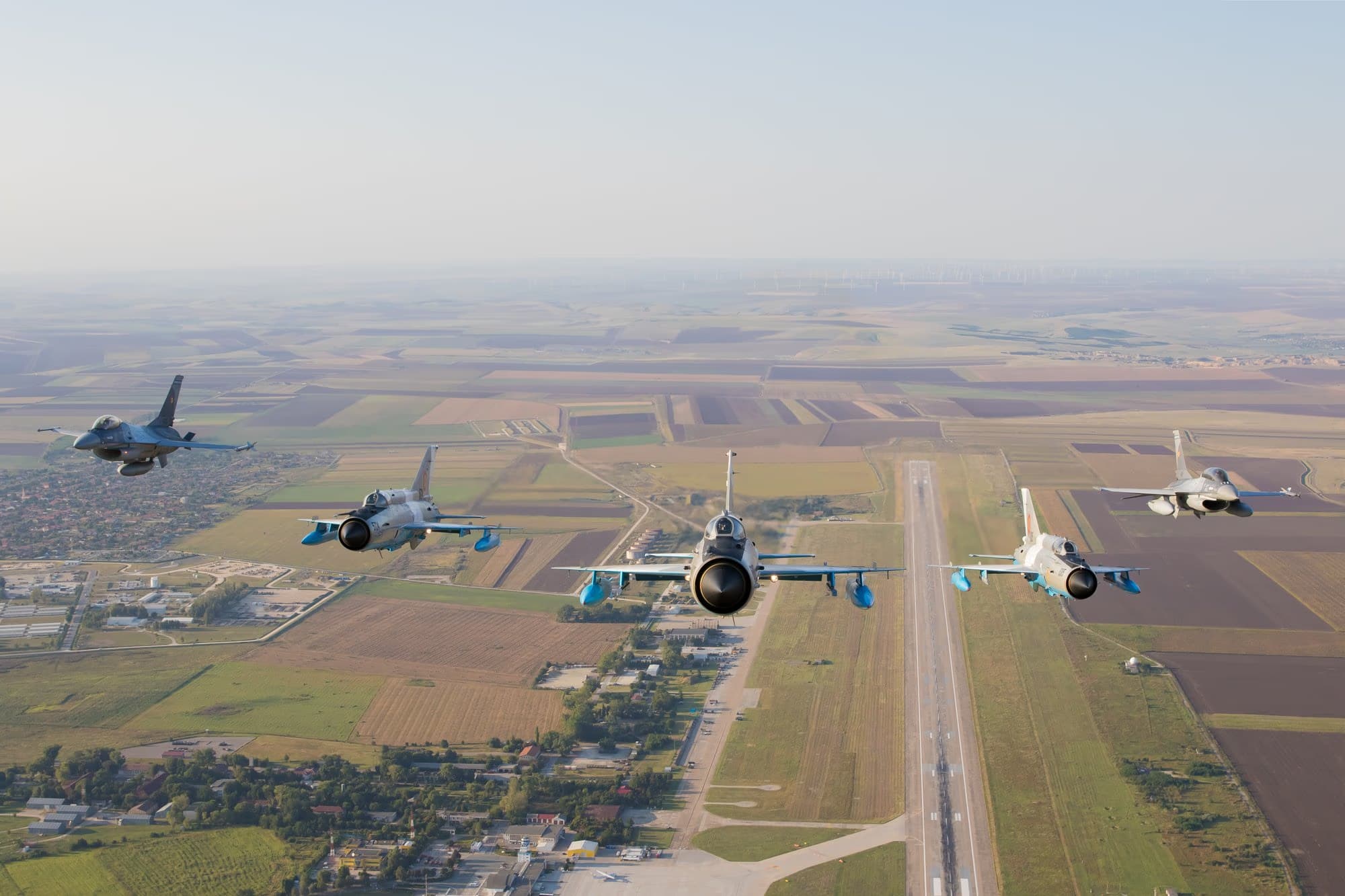 Öt román légierős F-16-os formációban repül egy leszállópálya felett, manőverezés közben
