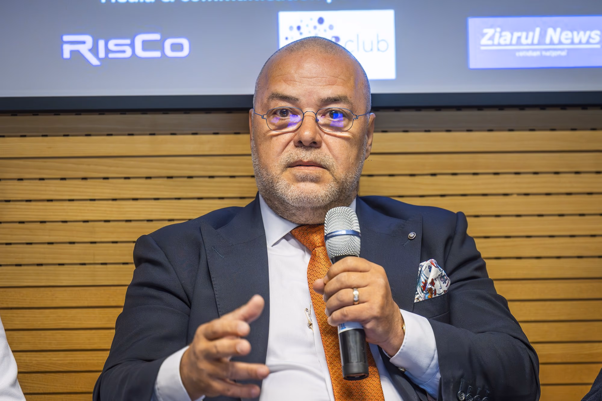 Florin Dănescu, Executive President of the Romanian Banking Association, speaking into the microphone, wearing an orange tie
