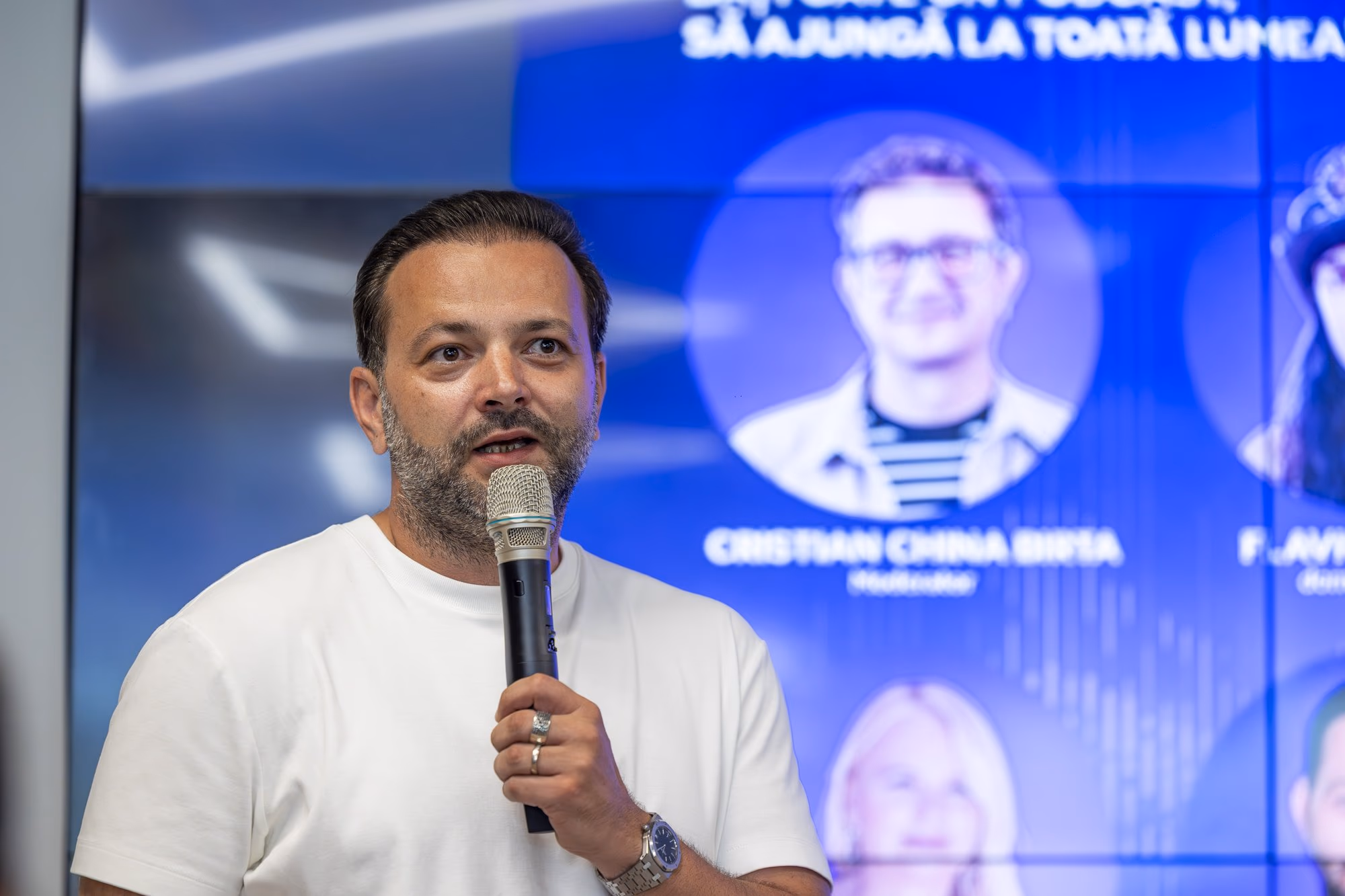 Mihai Morar at the microphone during panel 1, white shirt, with the ConfCast poster projected in the background.
