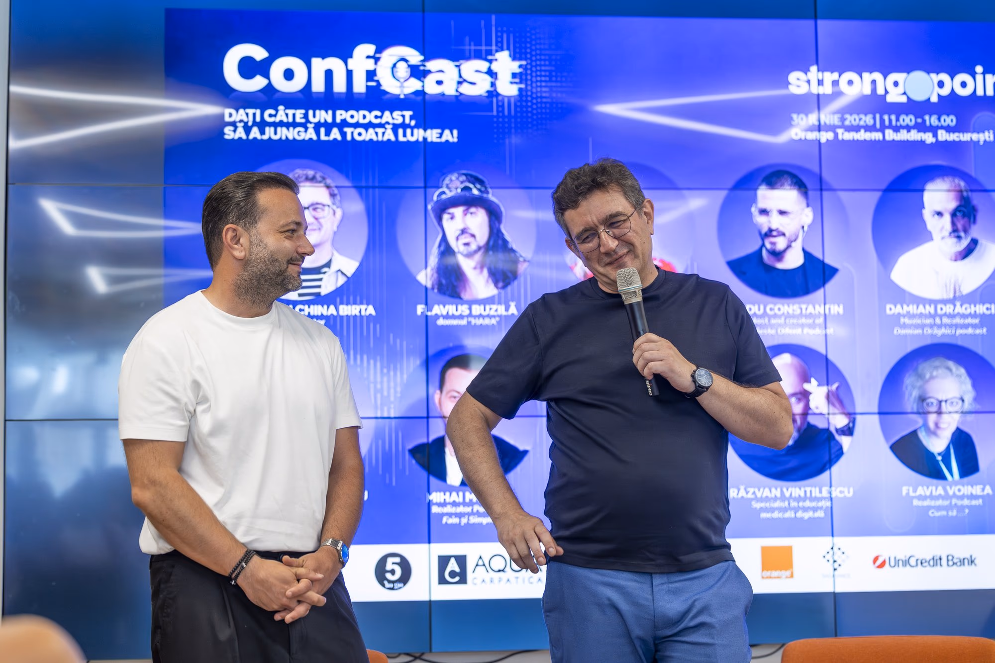 Cristian China Birta (Chinezu) and Mihai Morar open ConfCast in front of the poster of the ten podcasters, at the Orange Tandem hall, Bucharest, 30 June 2026.