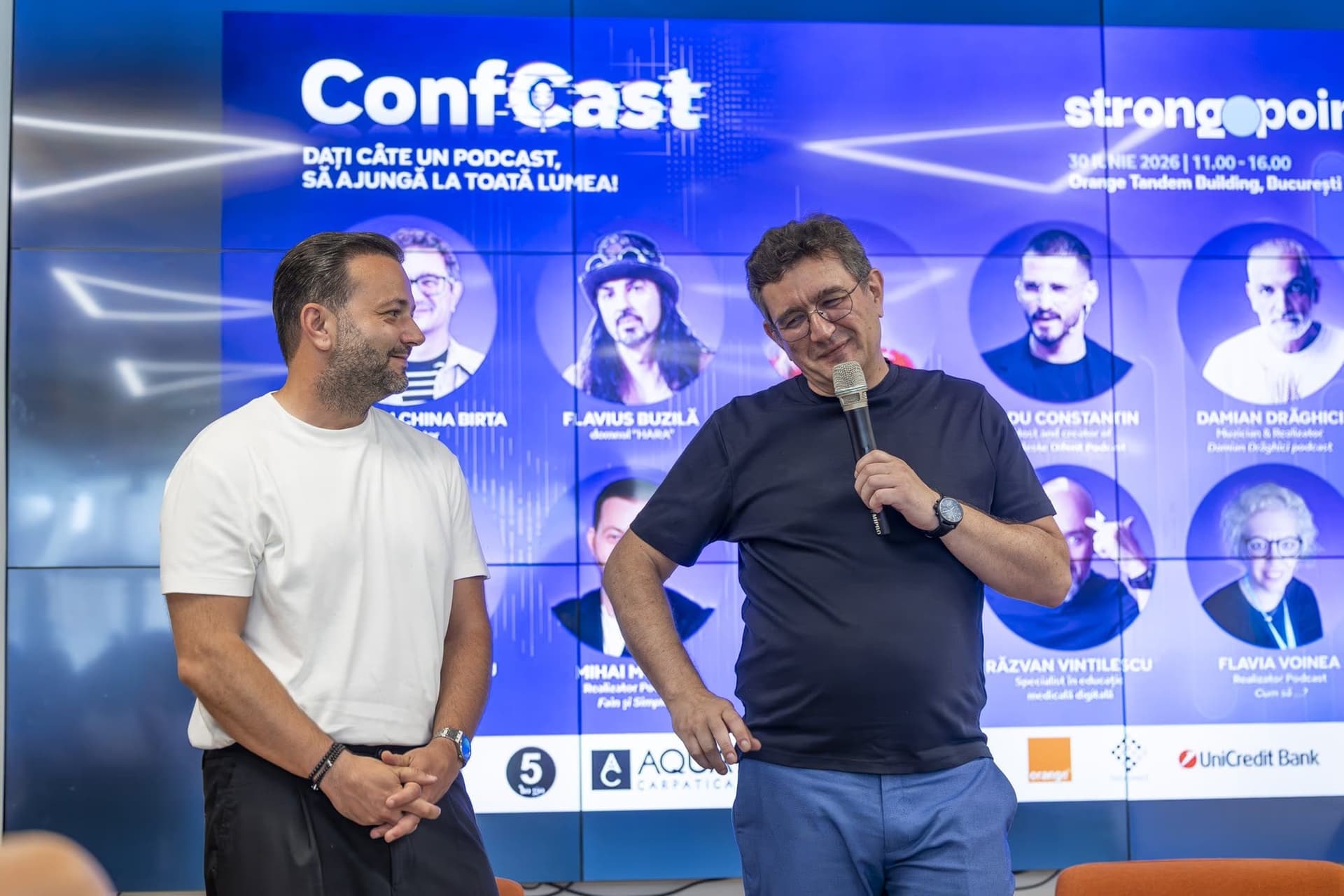 Cristian China Birta (Chinezu) és Mihai Morar megnyitja a ConfCastot a tíz podcastert bemutató plakát előtt, az Orange Tandem termében, Bukarest, 2026. június 30.
