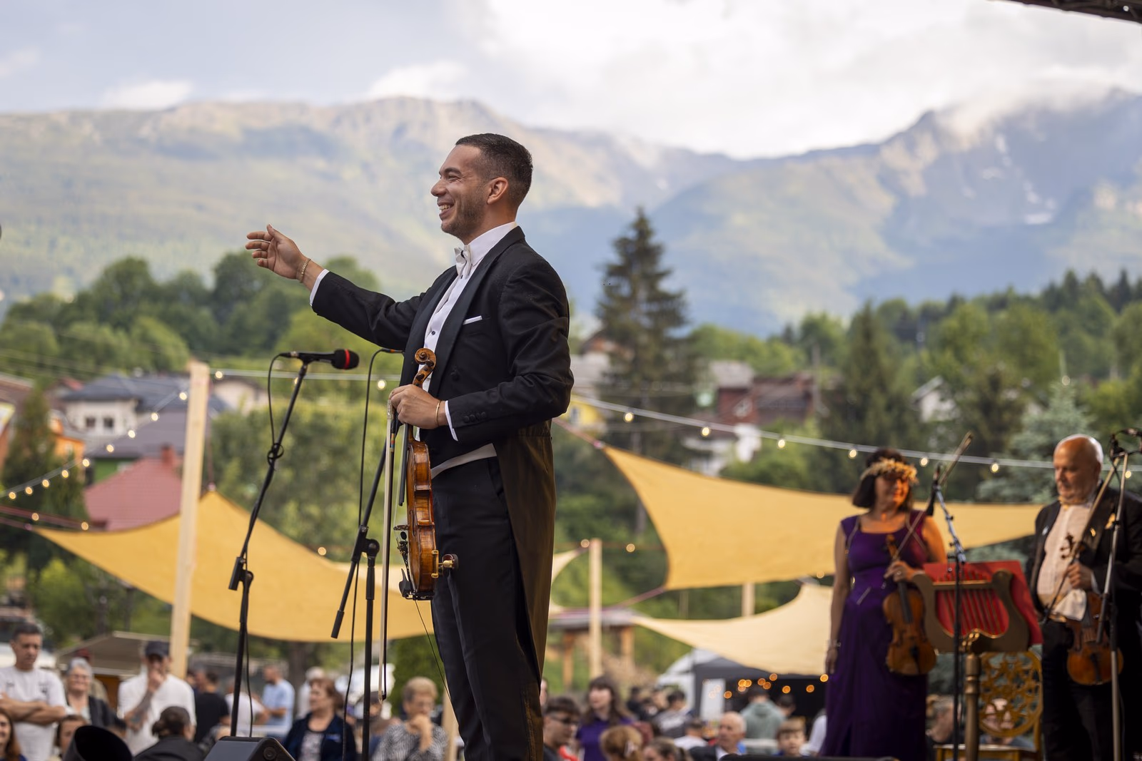 Dirijorul-violonist în frac pe scena în aer liber din Borșa, cu vioara în mână și Munții Rodnei în fundal, la concertul „Simfonia Iubirii"