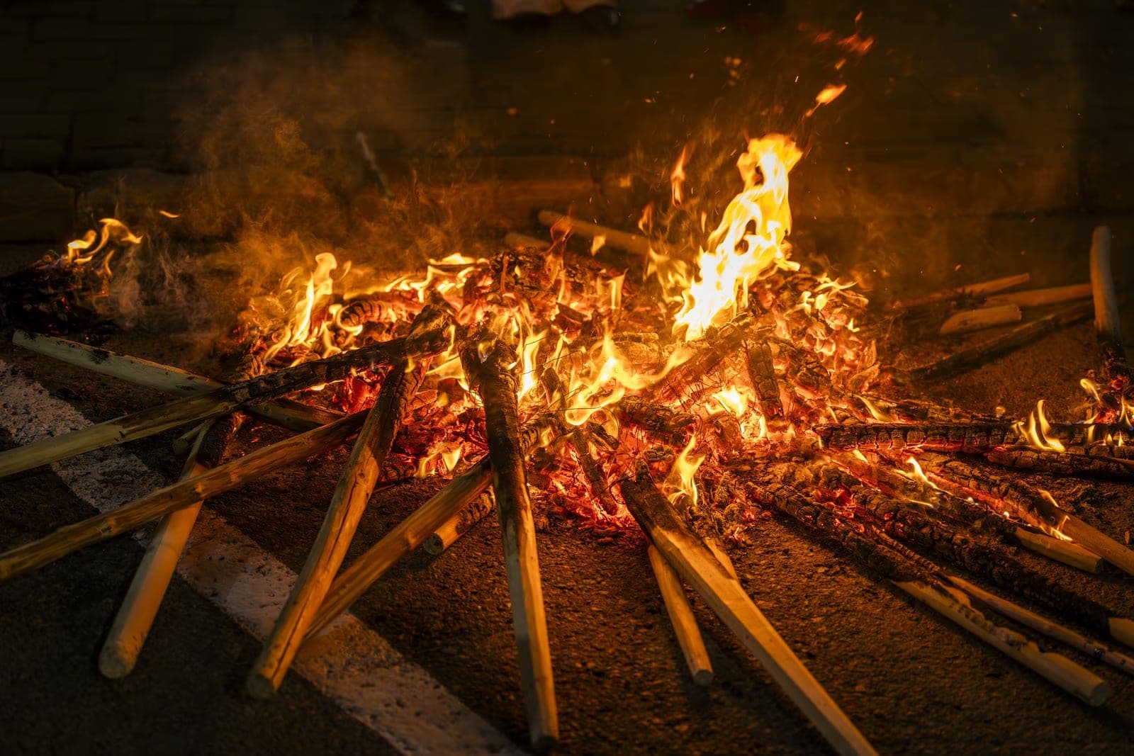 The embers of the Sânziene fire with the pale handles of the charred torches and visible wire remnants on the asphalt in Borșa
