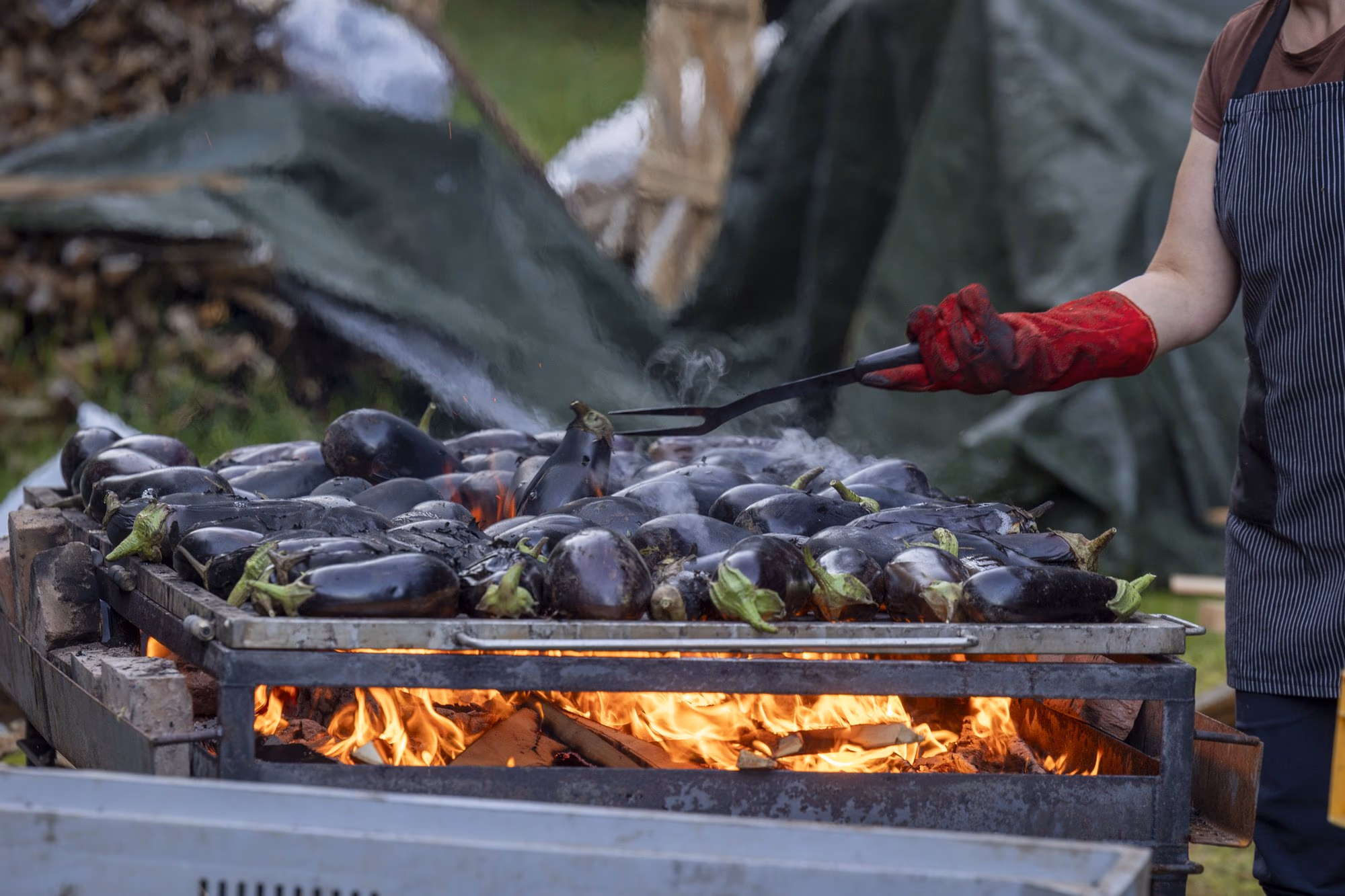 Woman turning the aubergines with tongs over the fire