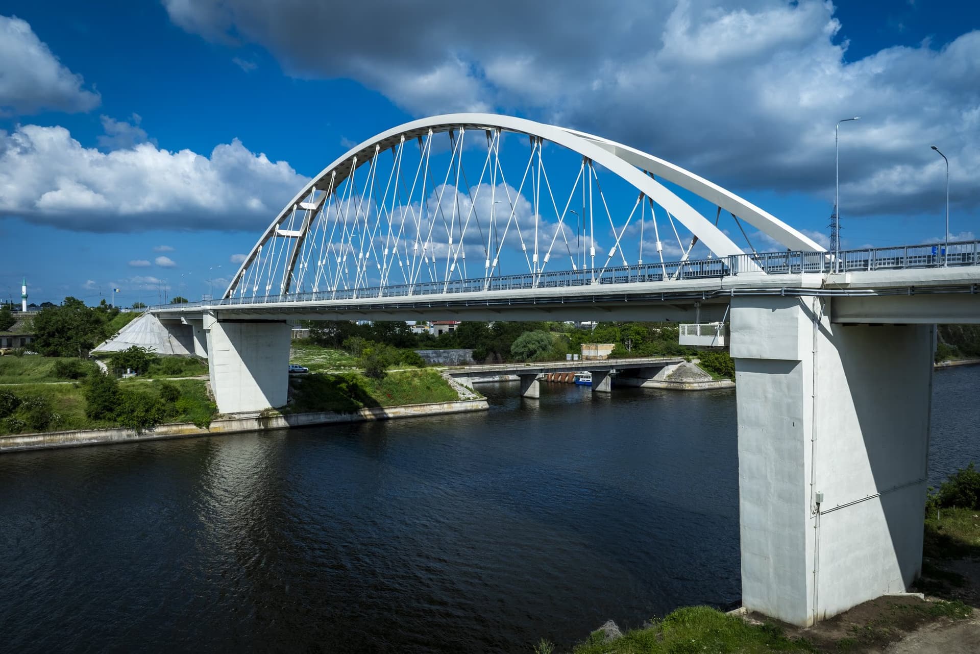 Side view of the bridge: the white steel arch and the approach viaducts over the canal