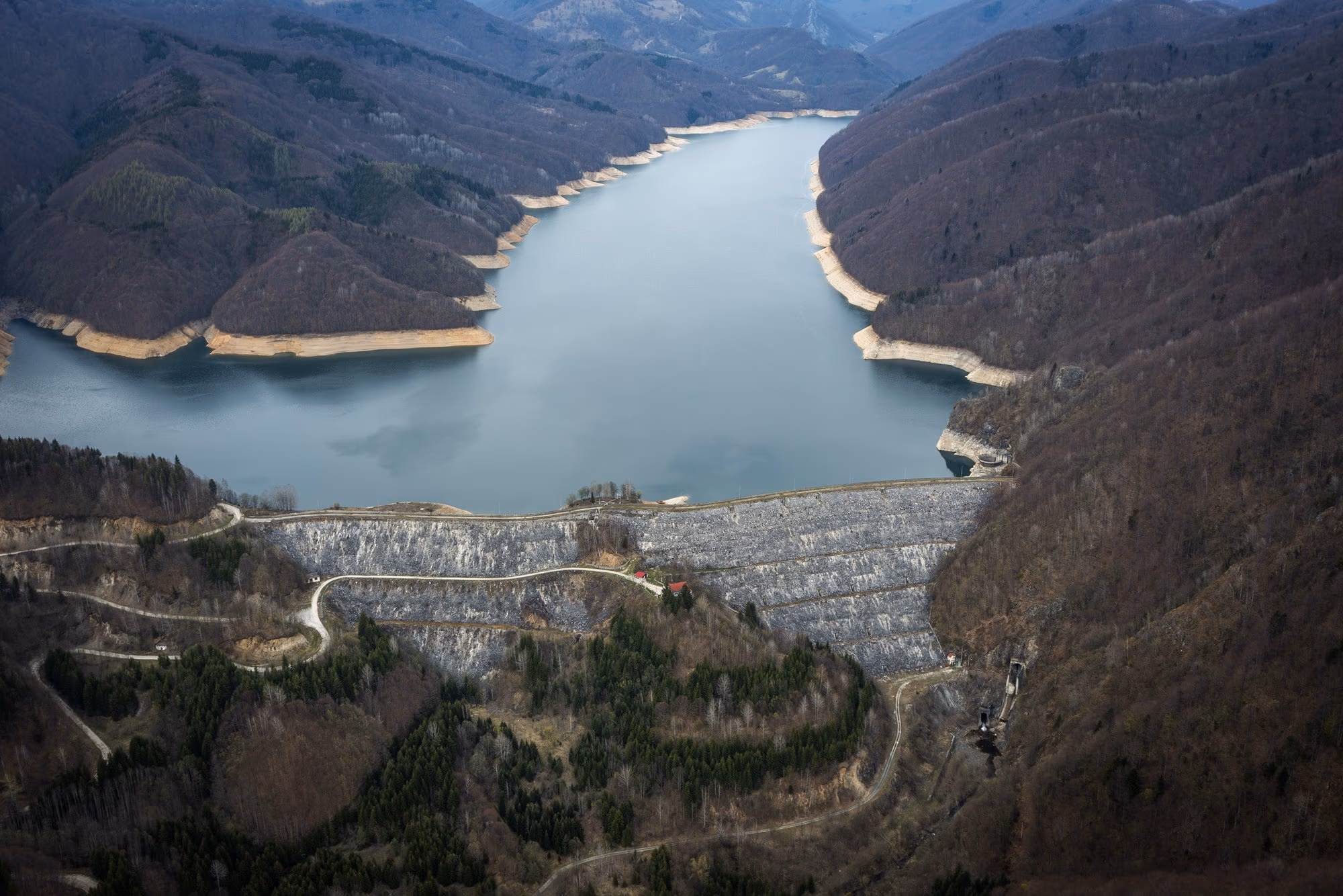 The Valea lui Iovan rockfill dam on the Cerna, with the reservoir drawn down and snow-covered mountains behind