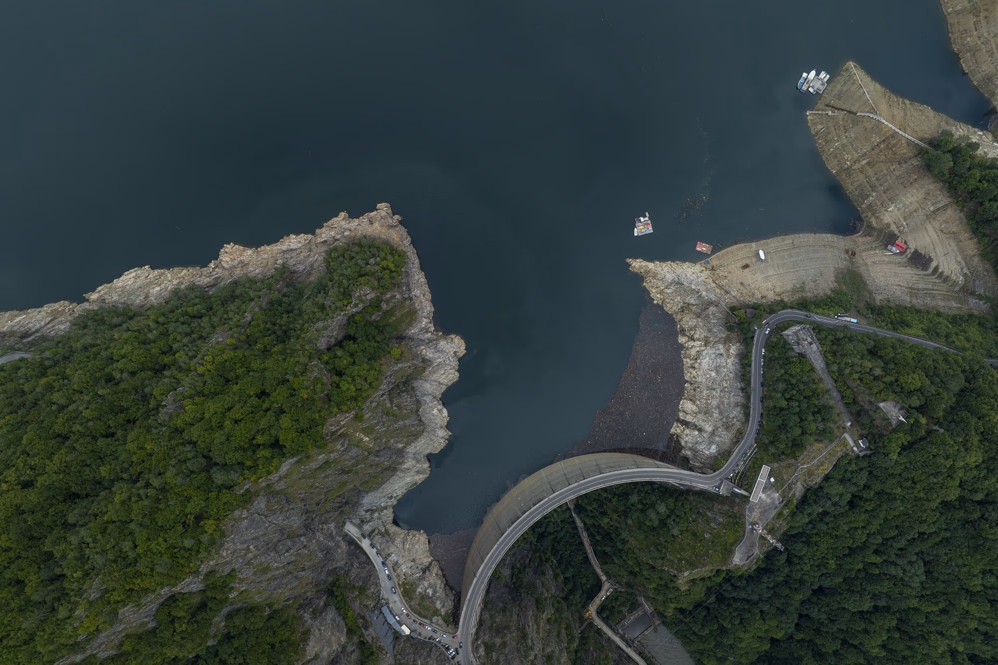 The exposed banks of Lake Vidraru seen almost vertically from a drone, with the access road winding along the shore