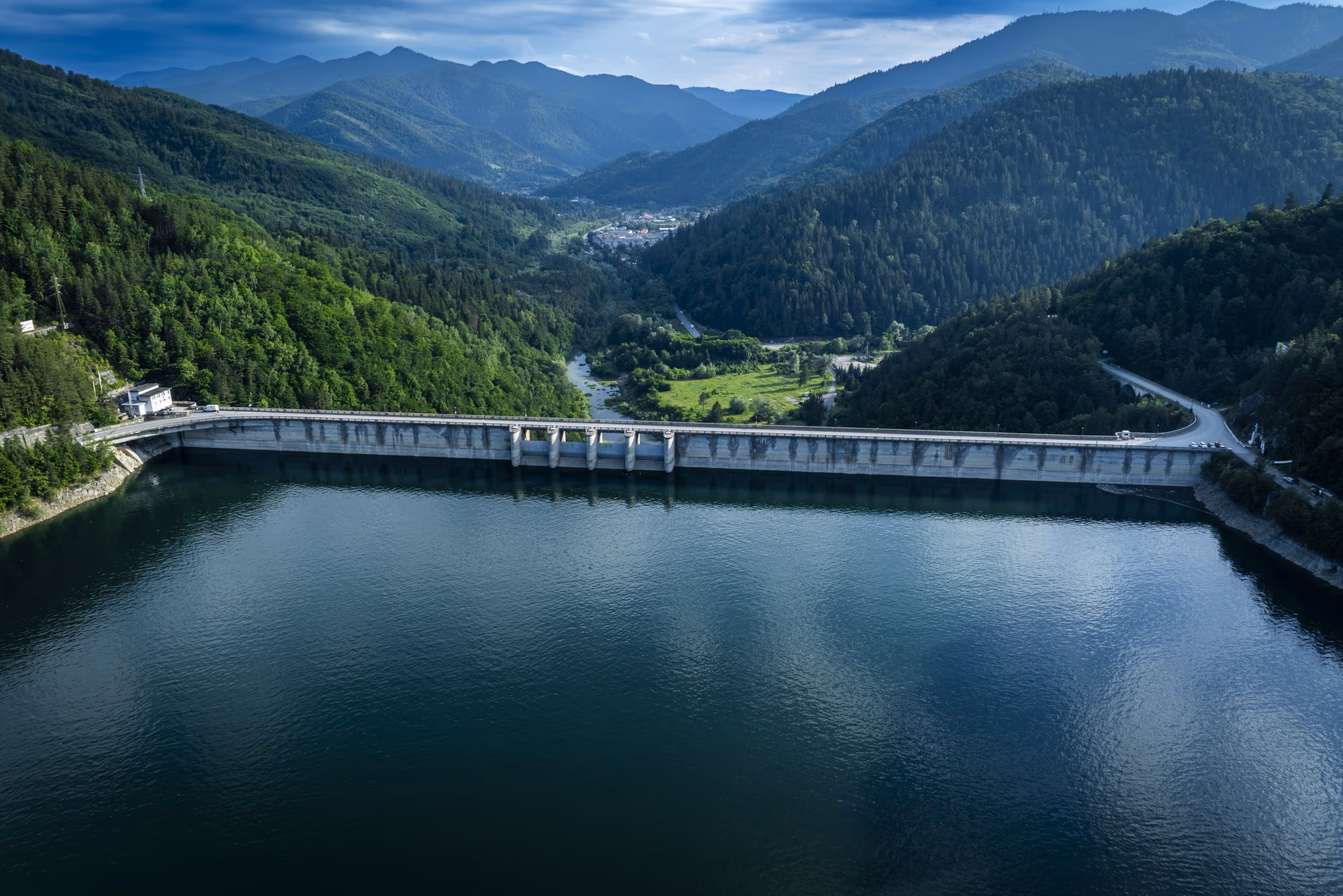Izvorul Muntelui dam seen from the lake, with its long crest and the Bistrița valley opening downstream