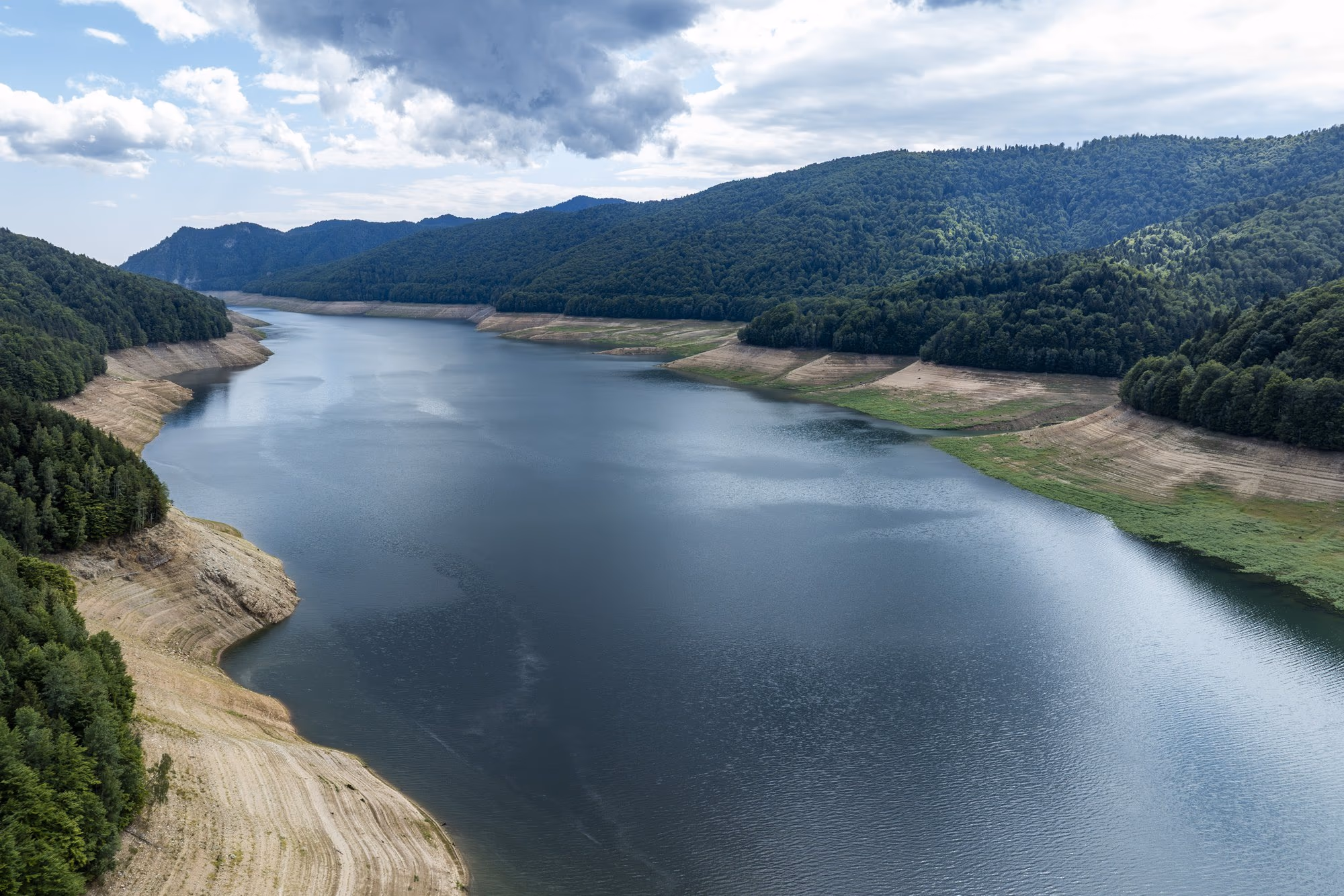 The Vidraru valley with the reservoir drawn down and tens of metres of exposed shoreline, seen from a drone