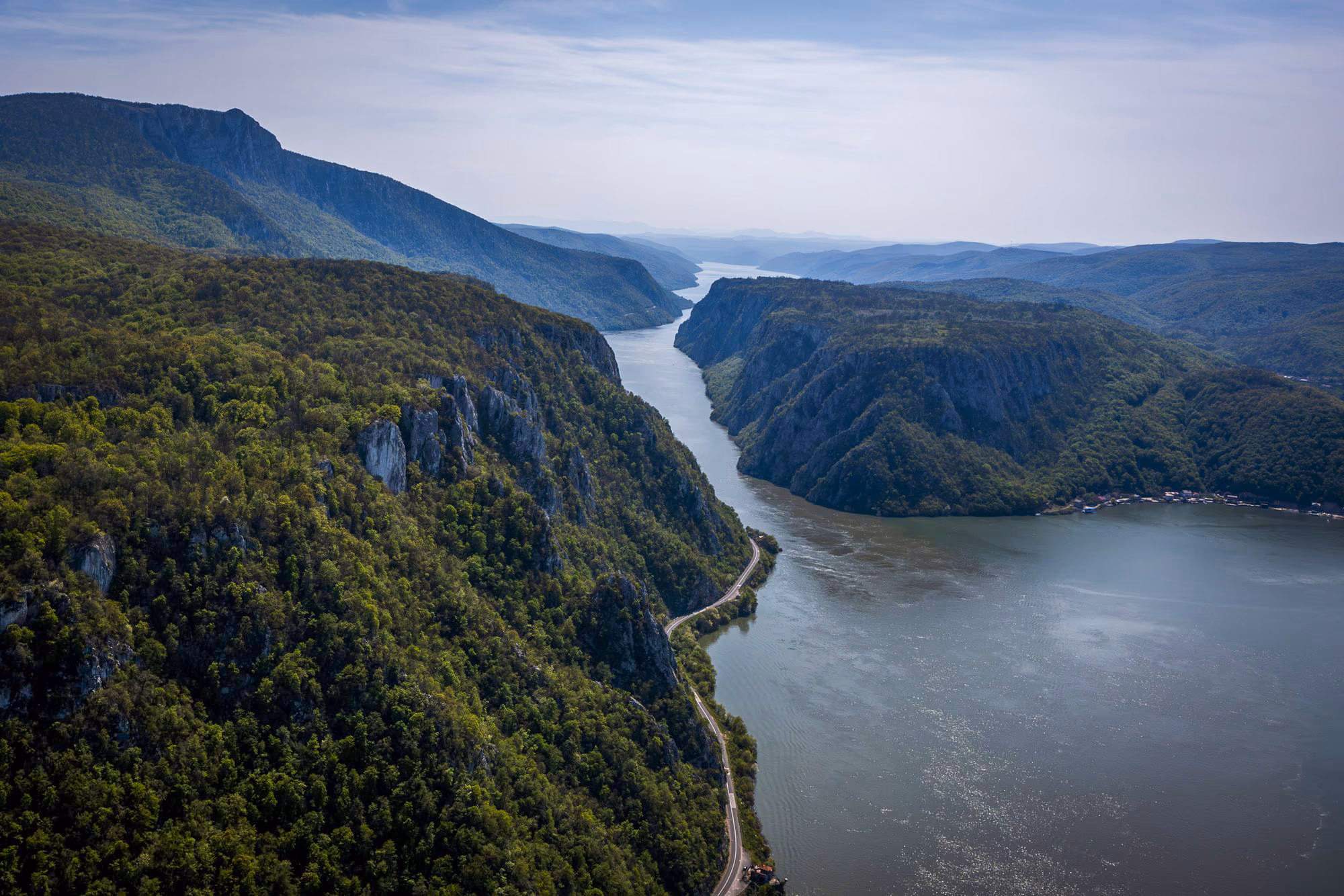 The Danube flowing through the gorge between steep wooded slopes, seen from a drone