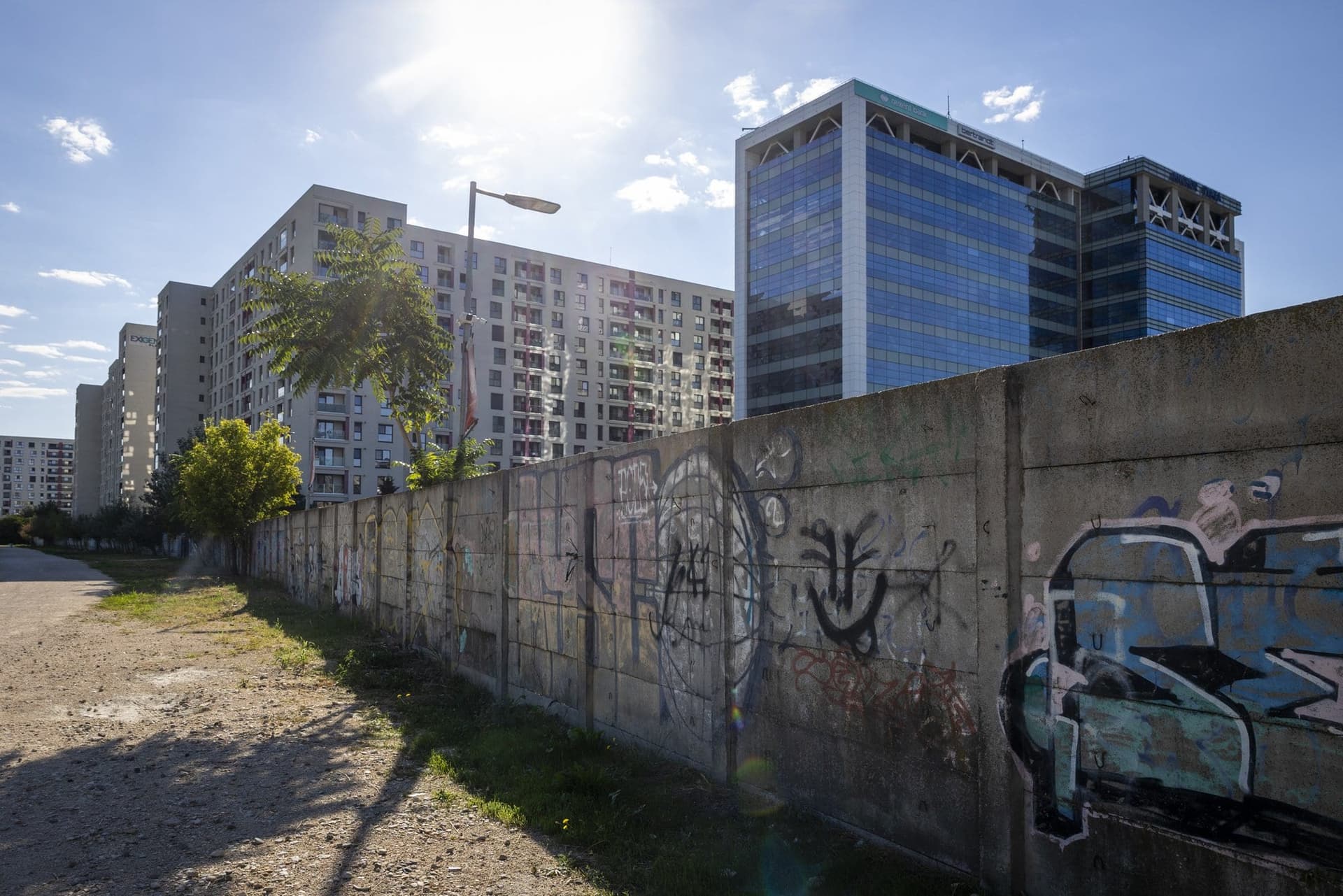 Gard de beton acoperit cu tag-uri, cu blocuri de locuințe și o clădire de birouri de sticlă în fundal