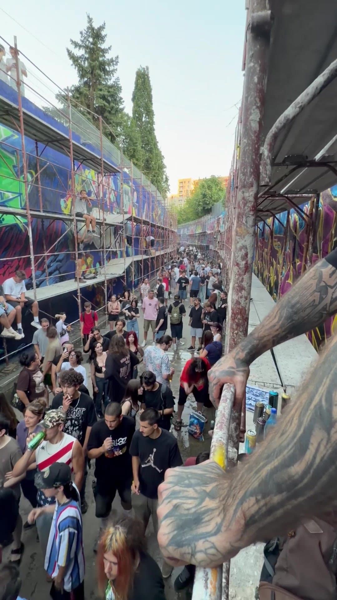 Pasajul plin de oameni, văzut de sus de pe schelă, cu brațul unui artist sprijinit de țeava din prim-plan