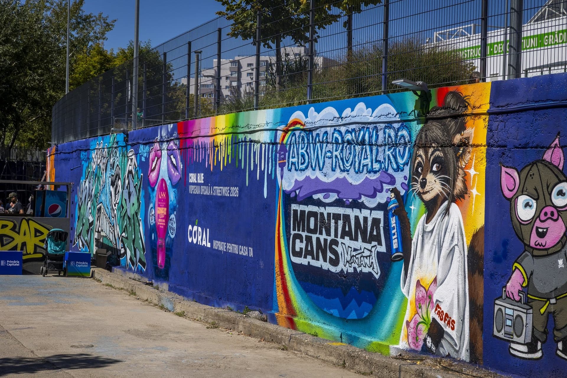 Porțiune de perete pictată cu numele sponsorilor, printre care „Coral Blue — vopseaua oficială a StreetWise 2026", lângă un bar improvizat