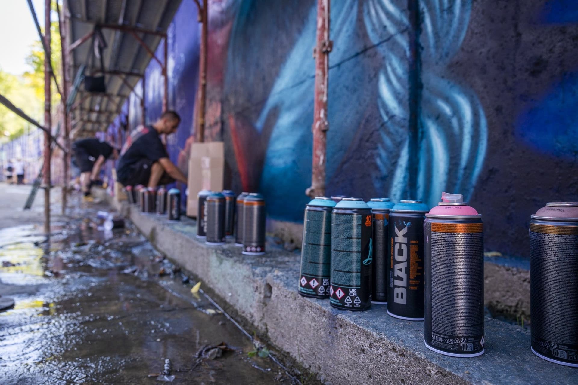 Doze de spray aliniate pe pragul de beton, în perspectivă, cu un artist care lucrează în plan secund