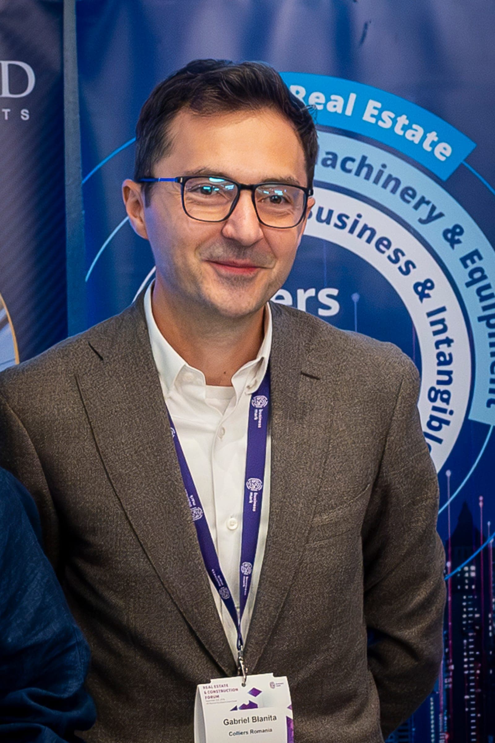 Gabriel Blăniță, in glasses, in front of the event banner