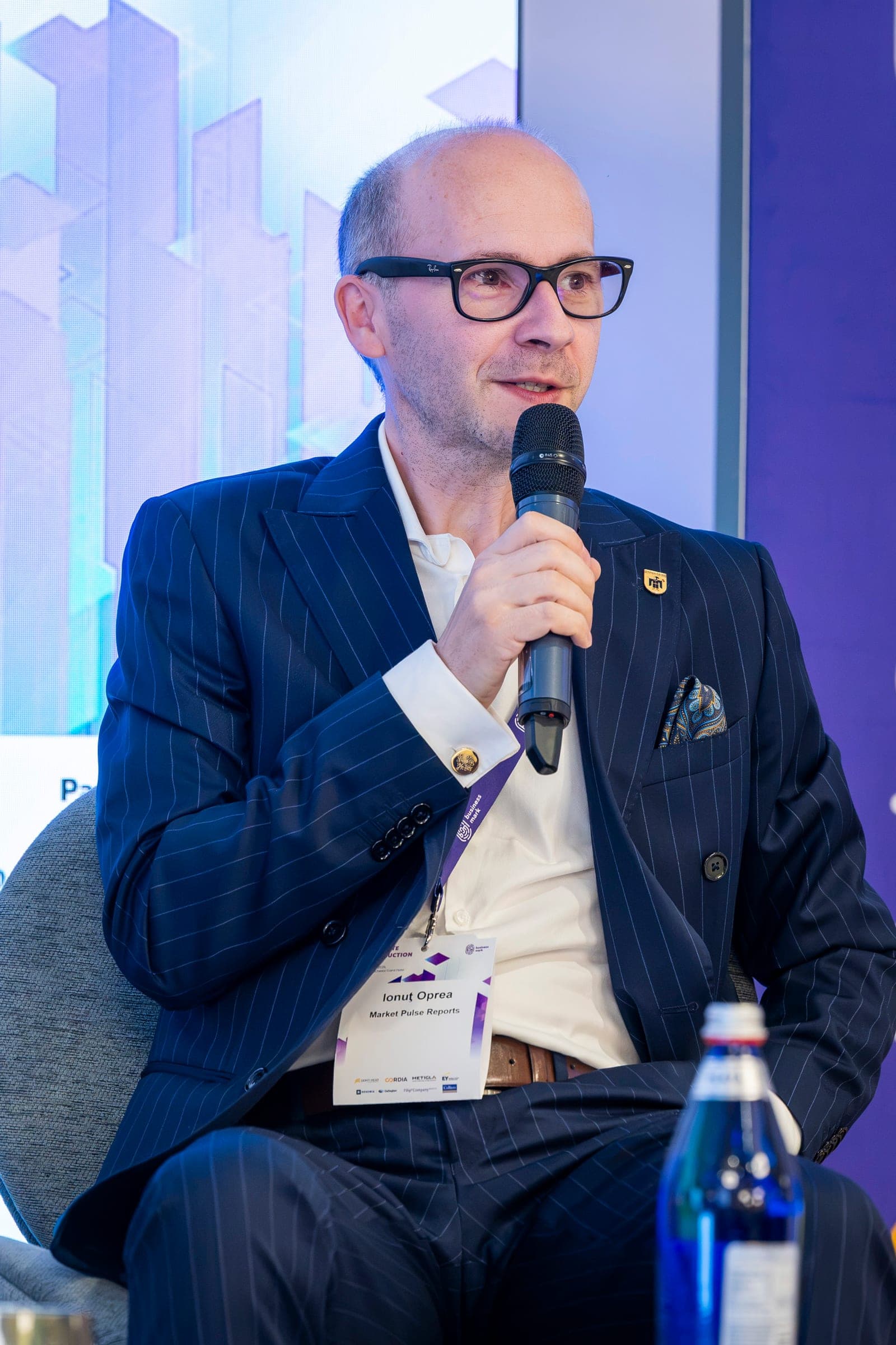 Ionuț Oprea, in glasses and a pinstripe suit, at the microphone