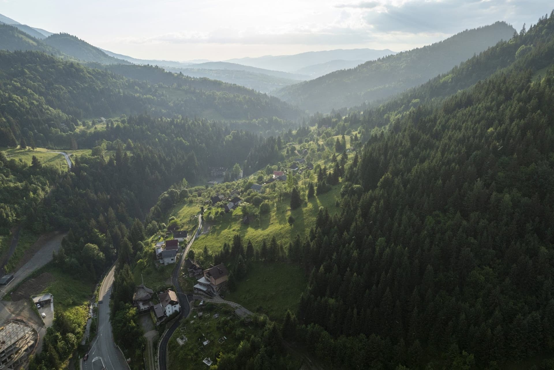 The valley around Borșa in evening light, with the road and scattered houses along the valley floor, photographed from a drone