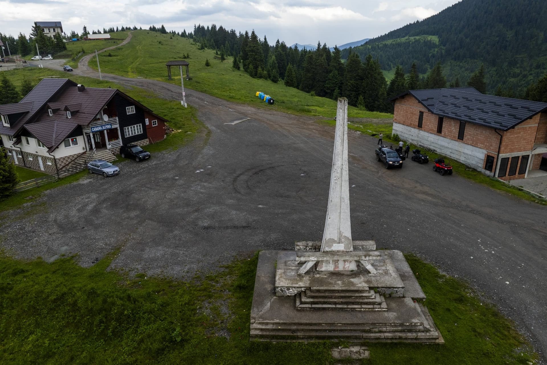 The concrete obelisk at the Prislop Pass, in a car park beside the Cabana Alpina, seen from a drone