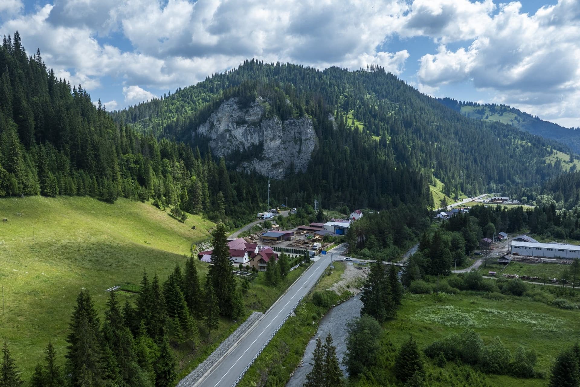 The DN18 in the Golden Bistrița valley at Cârlibaba, at the junction with the Țibău valley, with houses and a limestone crag, seen from a drone
