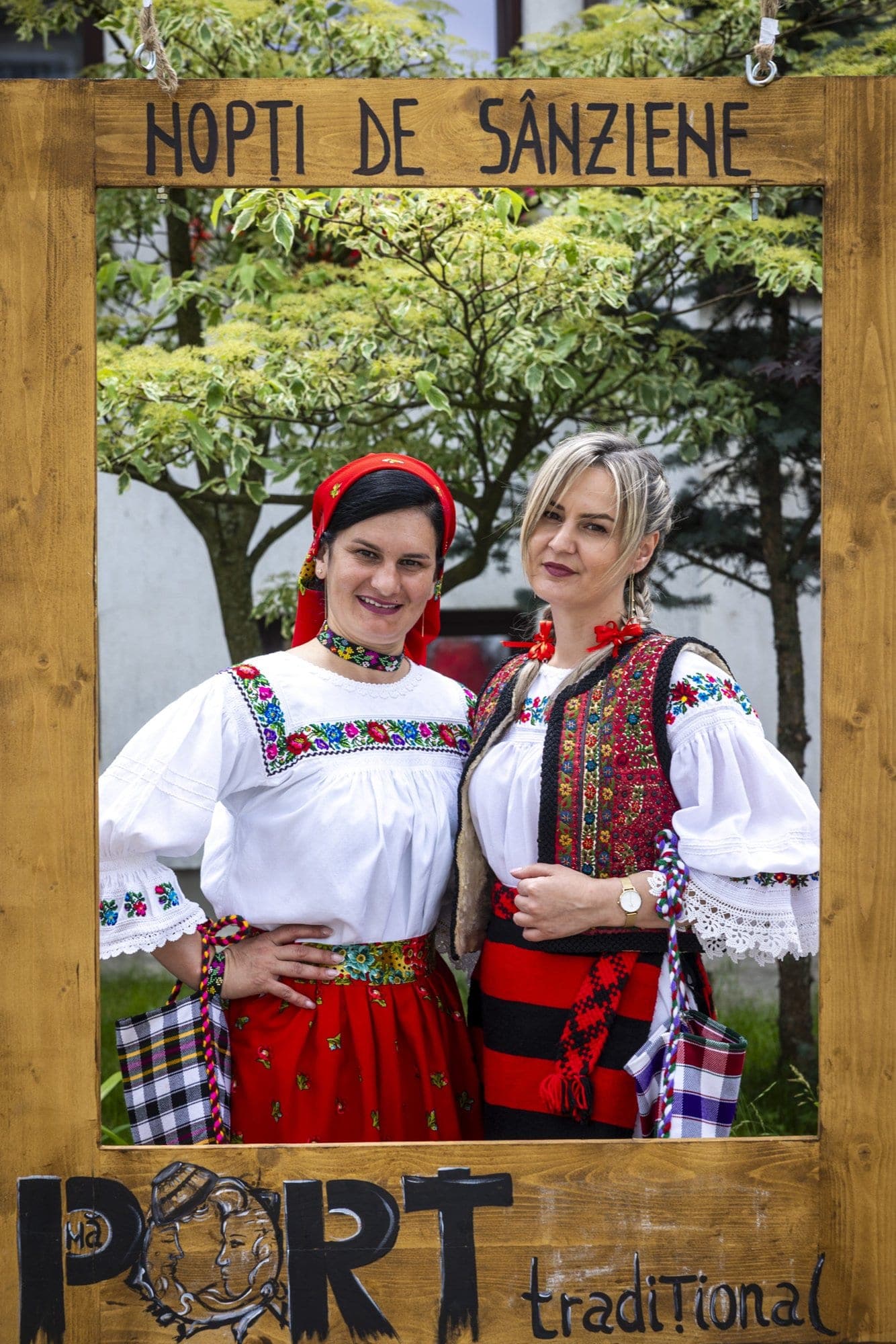 Two women in Maramureș folk costume inside a wooden frame reading "Nopți de Sânziene", in Borșa