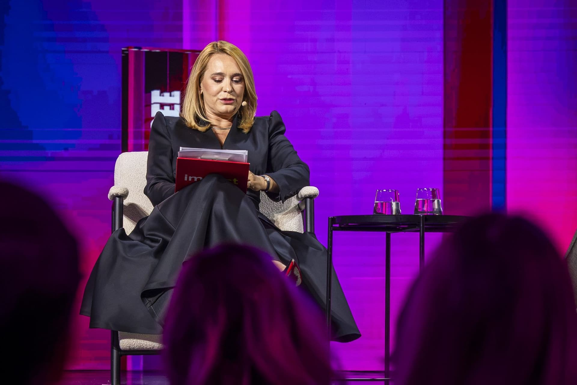 Andreea Esca, pe scena Impact SEE, citind dintr-un dosar roșu cu sigla conferinței, văzută din sală
