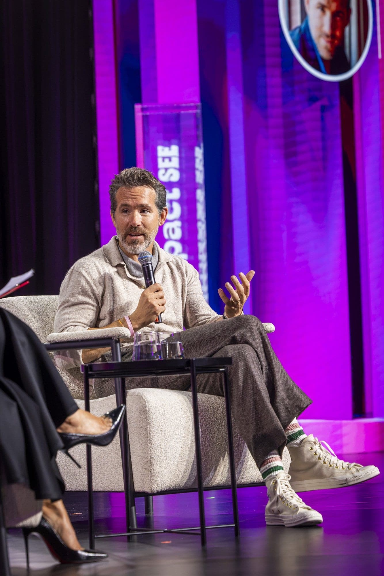 Ryan Reynolds, așezat în fotoliu pe scena Impact SEE, vorbind cu microfonul în mână, cadru vertical