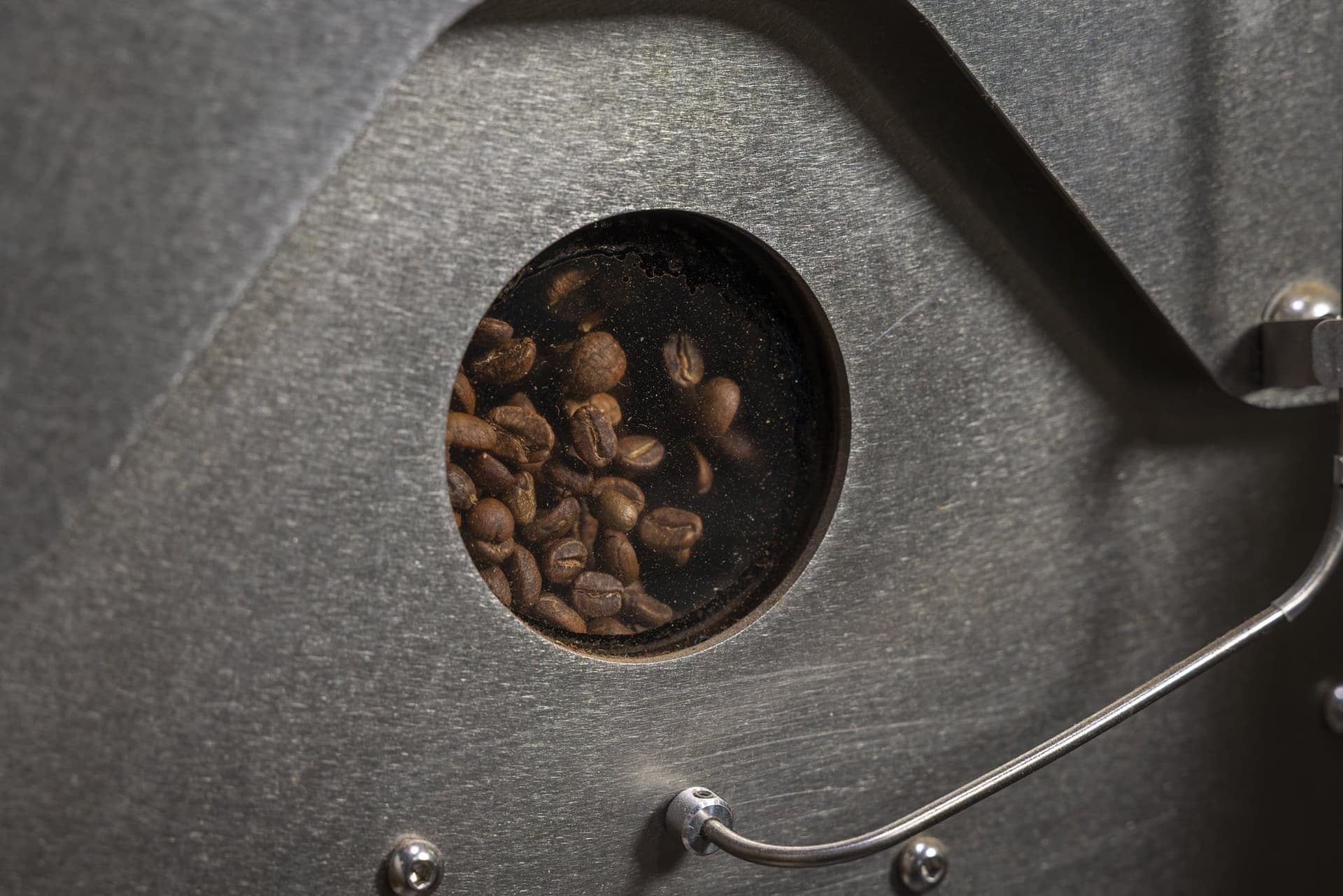 Boabe de cafea văzute prin fereastra rotundă a tamburului prăjitorului