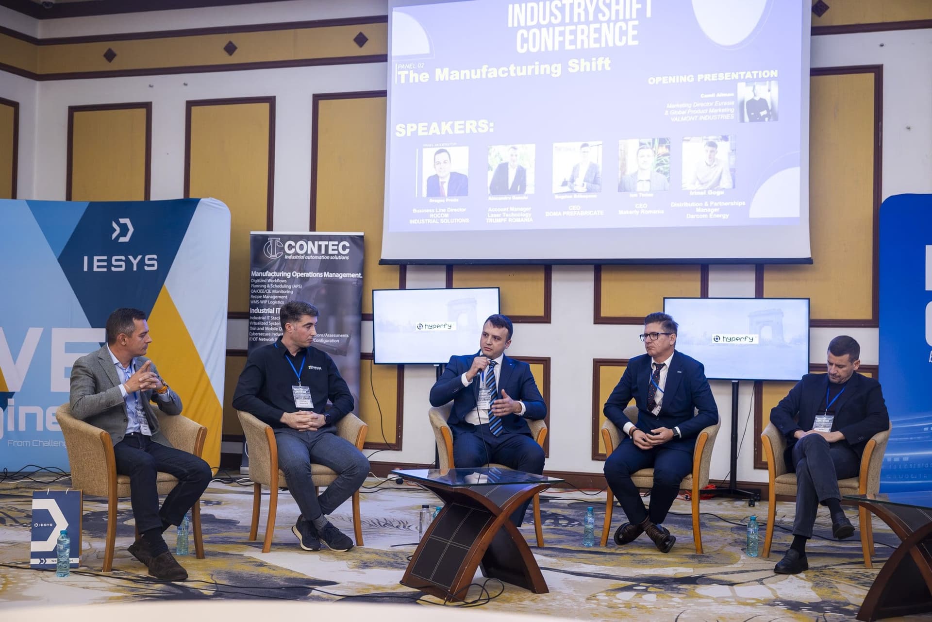 Cinci vorbitori pe scenă la panelul The Manufacturing Shift, cu ecranul conferinței în fundal