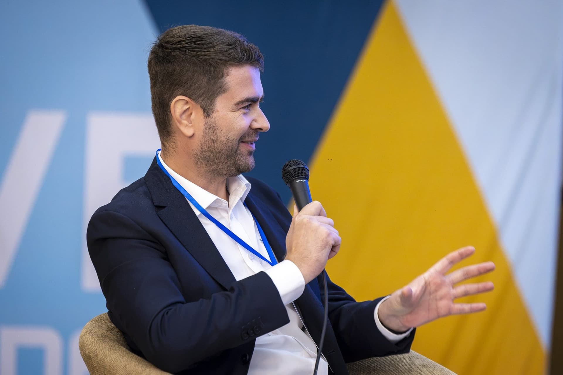 Răzvan Isac, de la Teradyne Robotics, vorbește la microfon, cu panoul unui sponsor în fundal