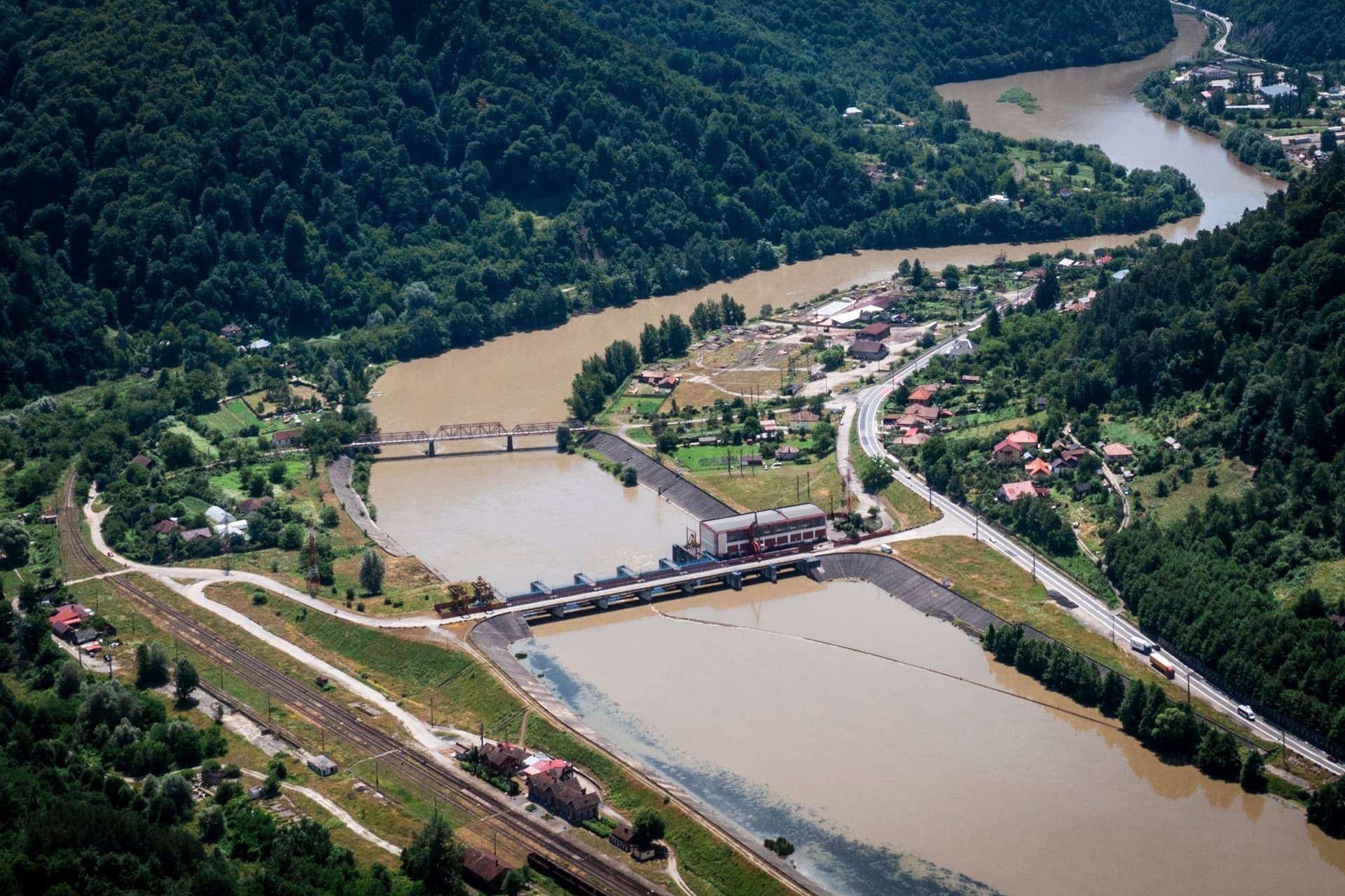 Barajul și centrala Gura Lotrului de la Brezoi văzute din aer, cu lacul în prim-plan, râul în aval, calea ferată și DN7 pe maluri