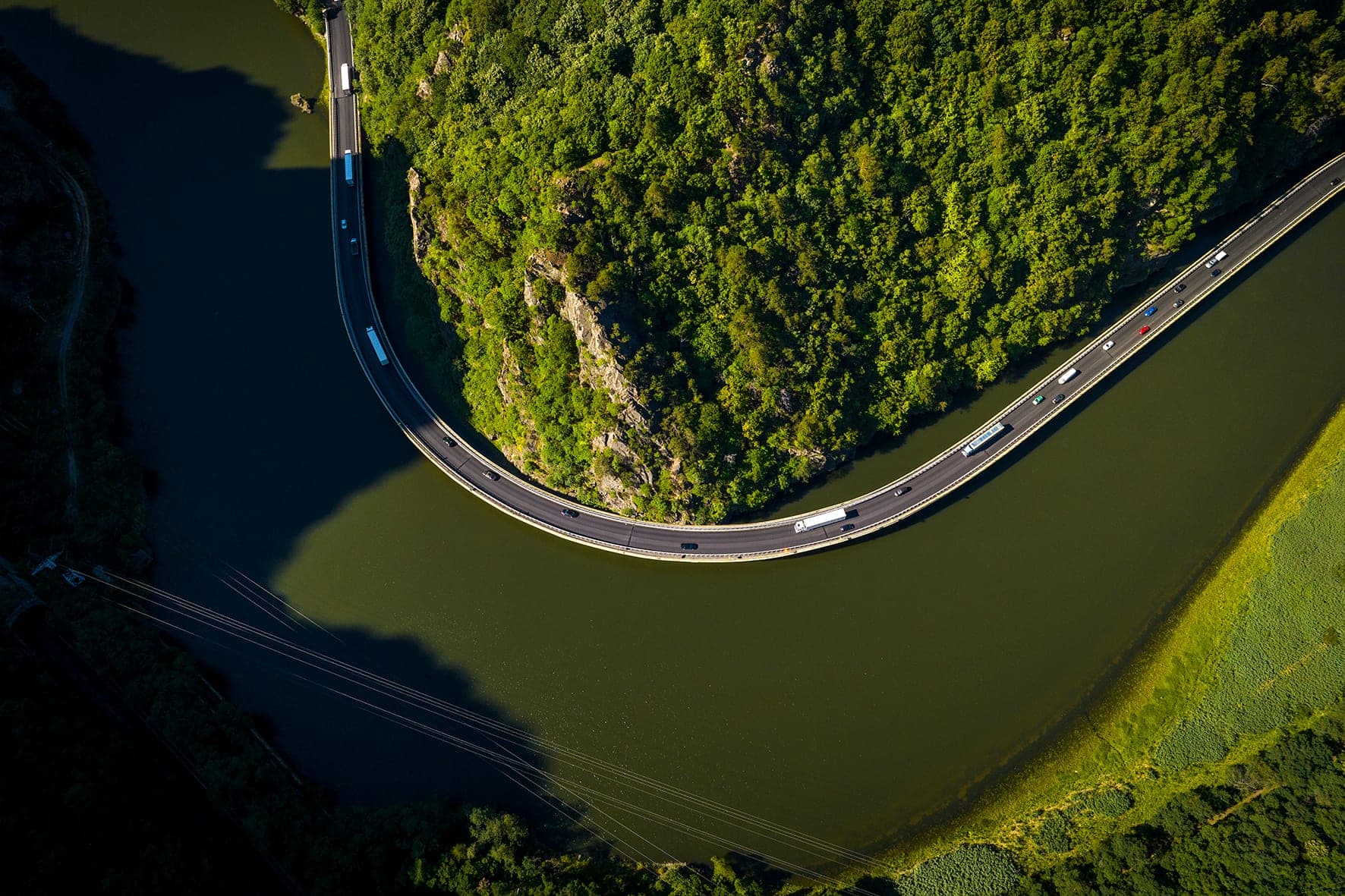 DN7 pe viaduct, urmând în curbă strânsă cotul Oltului, văzut de sus, ca de o pasăre, cu liniile de înaltă tensiune traversând apa