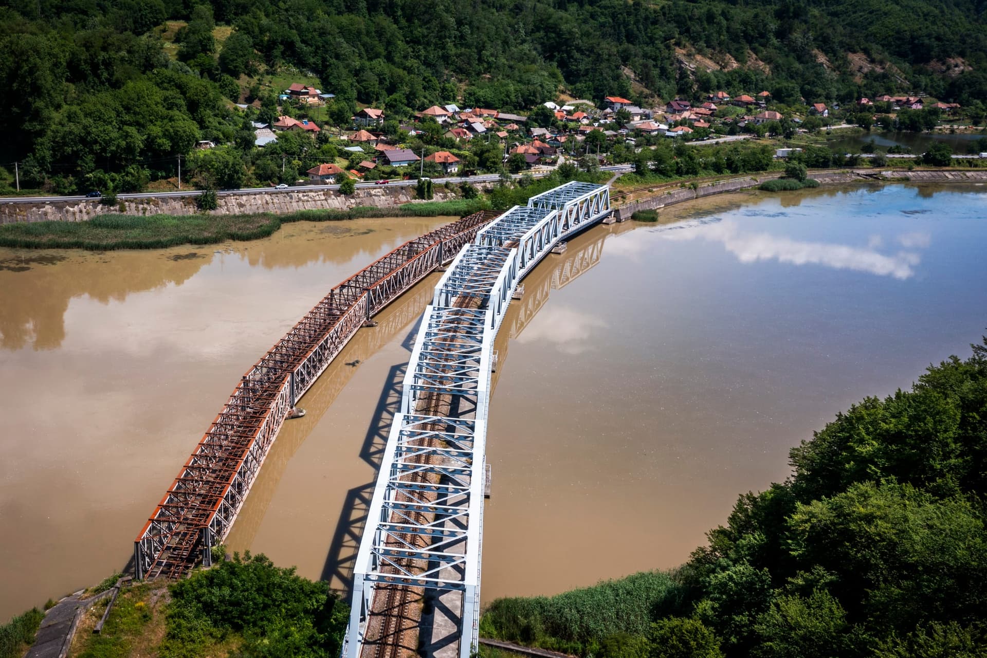 Podul vechi și ruginit de cale ferată de la Proieni, iar alături podul nou, vopsit în alb, pe care trece azi trenul, văzute de sus peste Olt